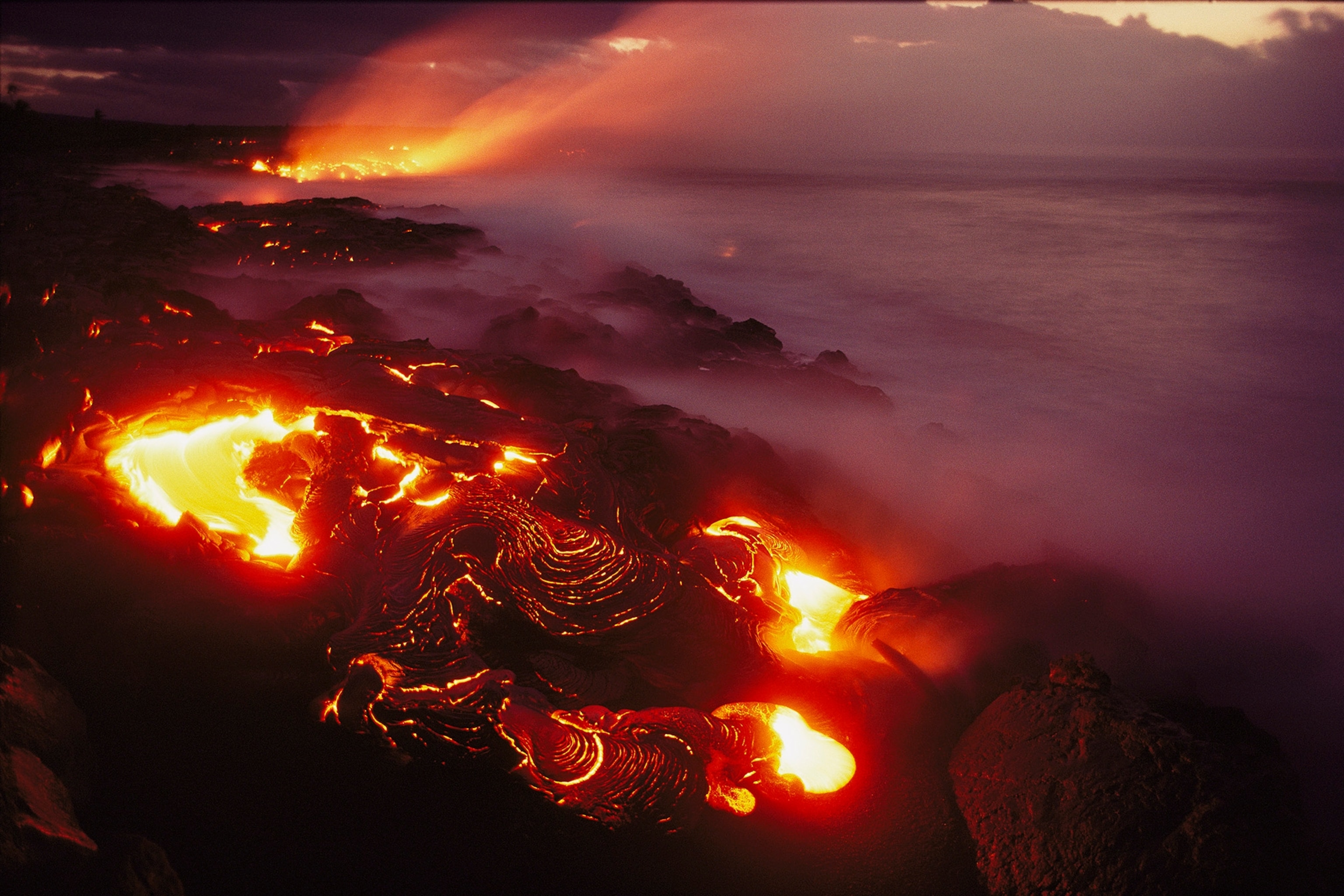 Lava flows white hot over black rock as a layer of steam rises