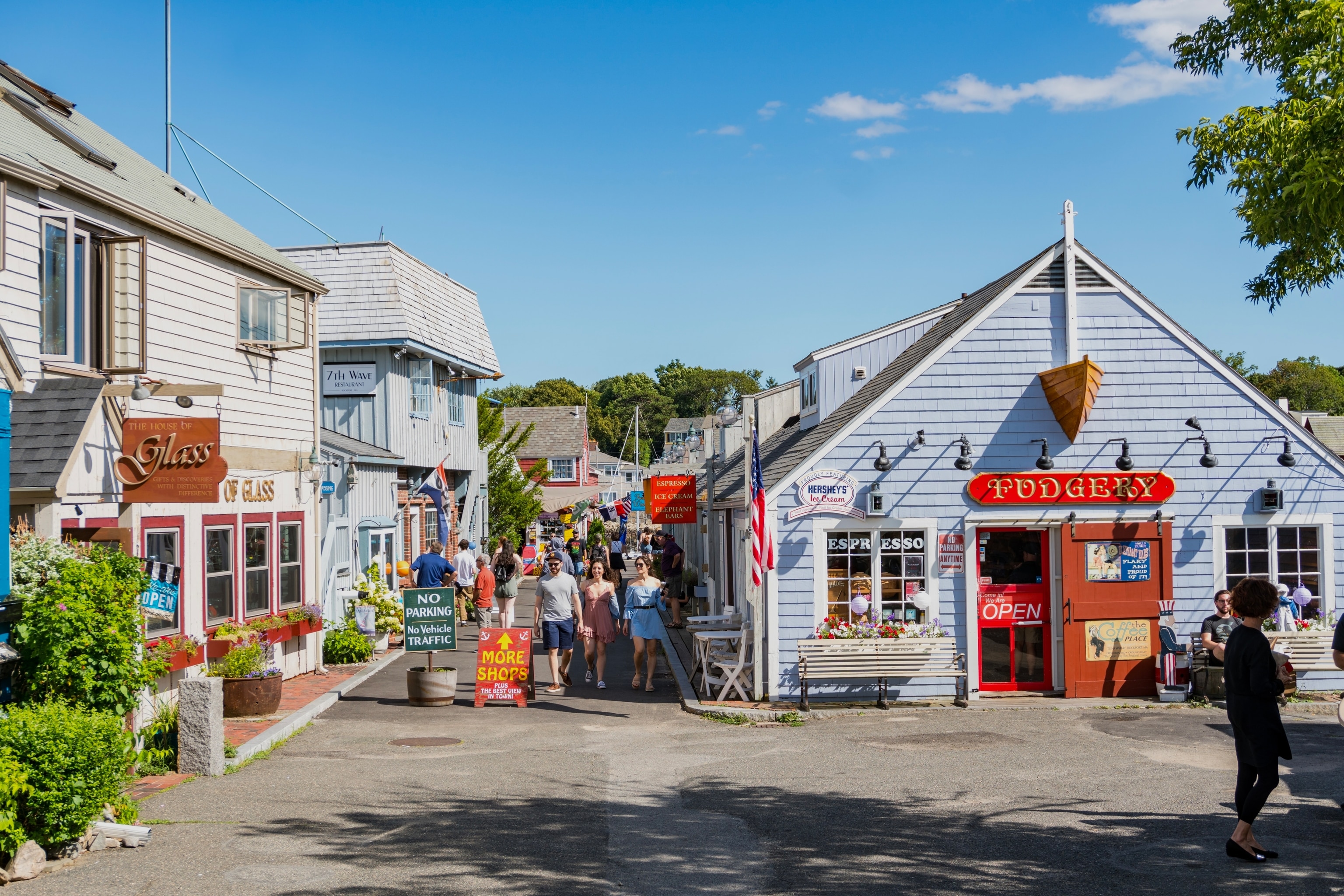 Crowds of people walk down the streets of Rockport, passing by shops on a sunny day.