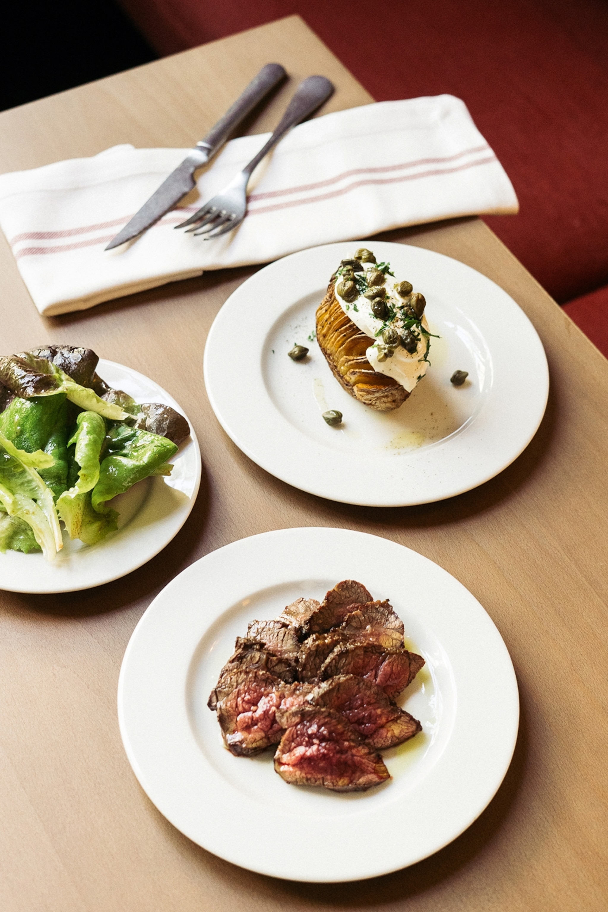 A sleek wooden table set with simple small plates, including a hassle back potato topped with yoghurt and capers.