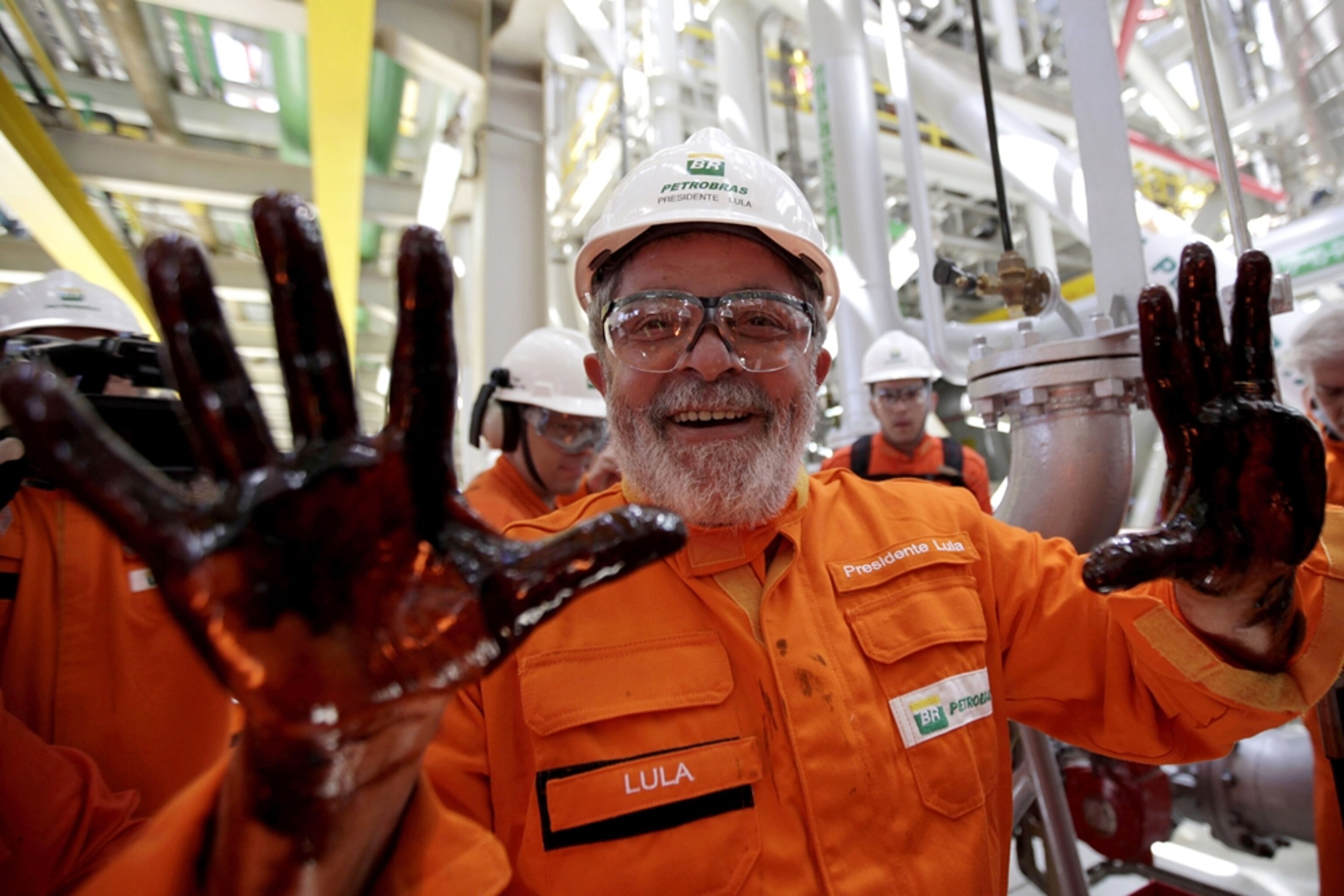Brazil's former president smiles at the camera as he holds up hands blacked with oil from a deepwater well