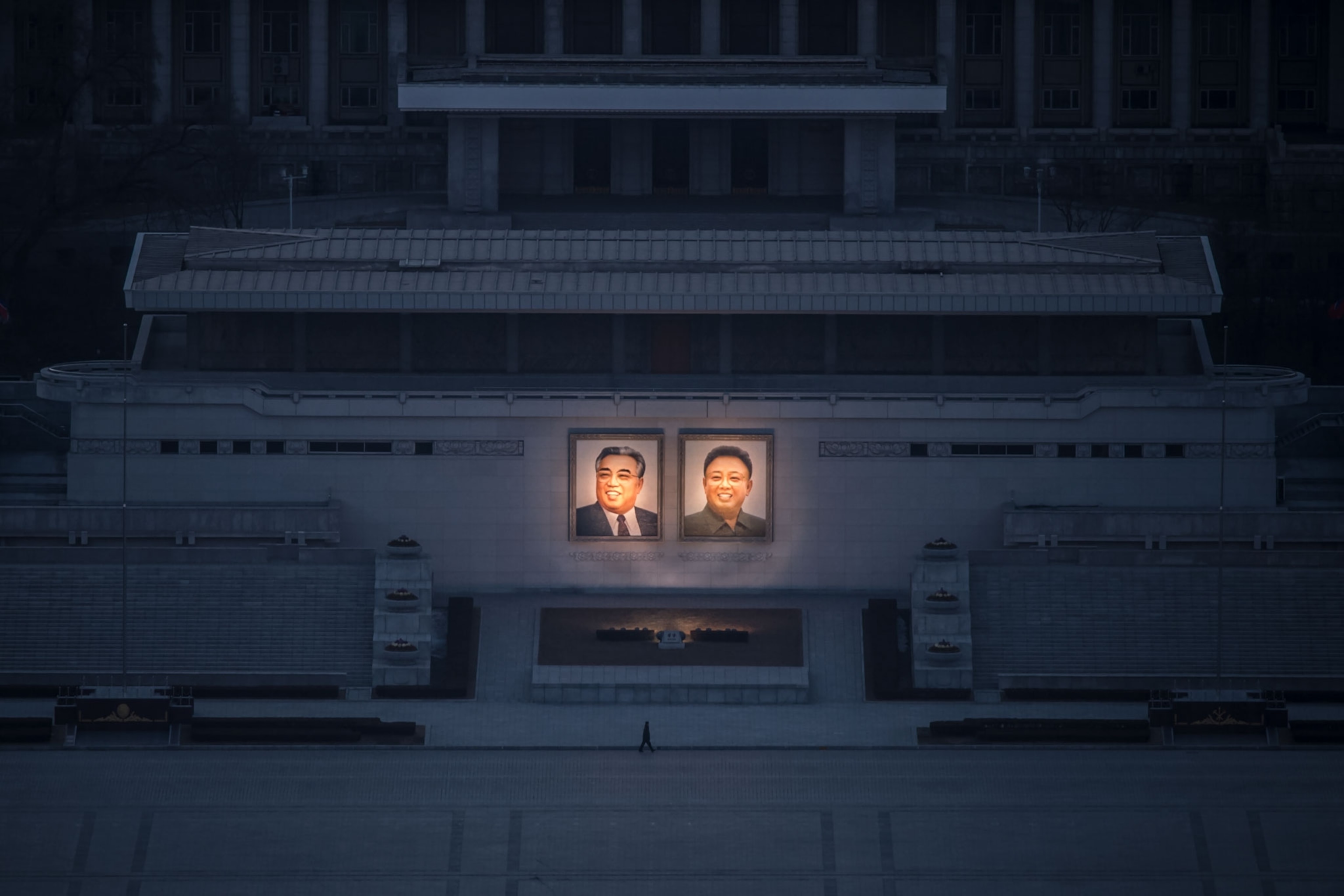 a person passing portraits of North Korean leaders Kim Il-Sung and Kim Jong-Il