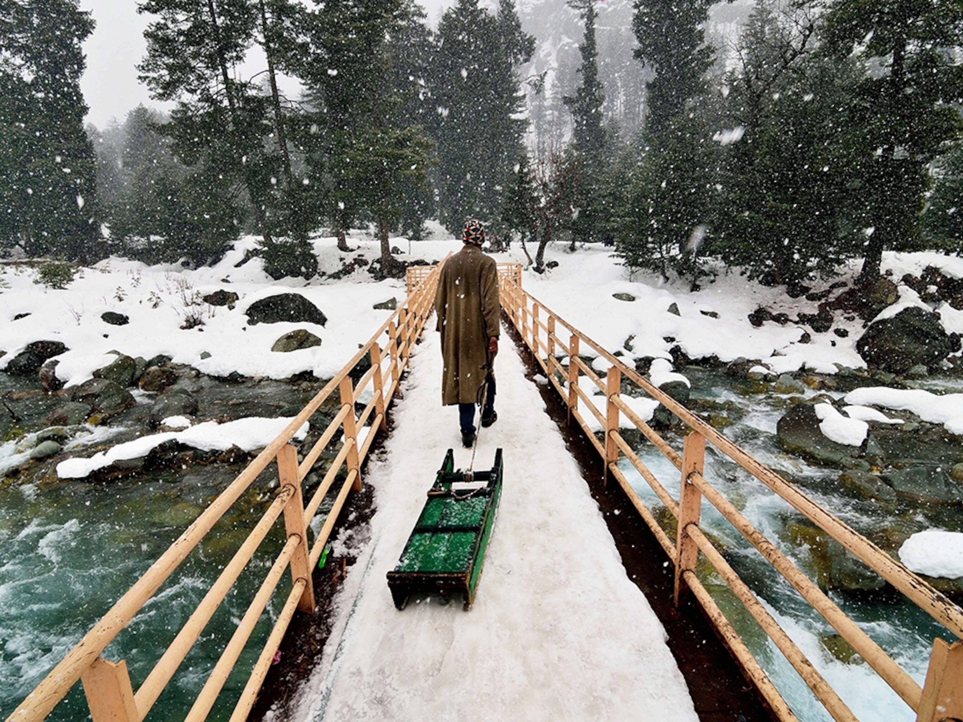 a man walking over a snowy bridge in Kashmir