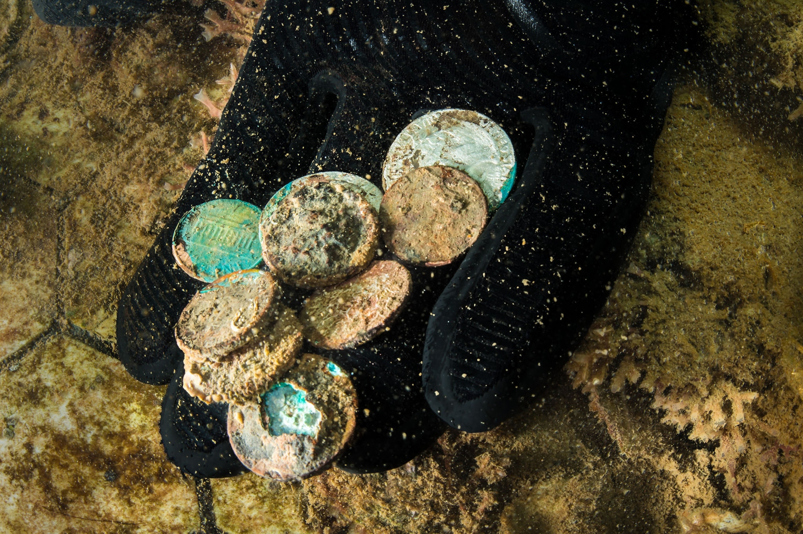 rusted coins in the hands of a diver under water