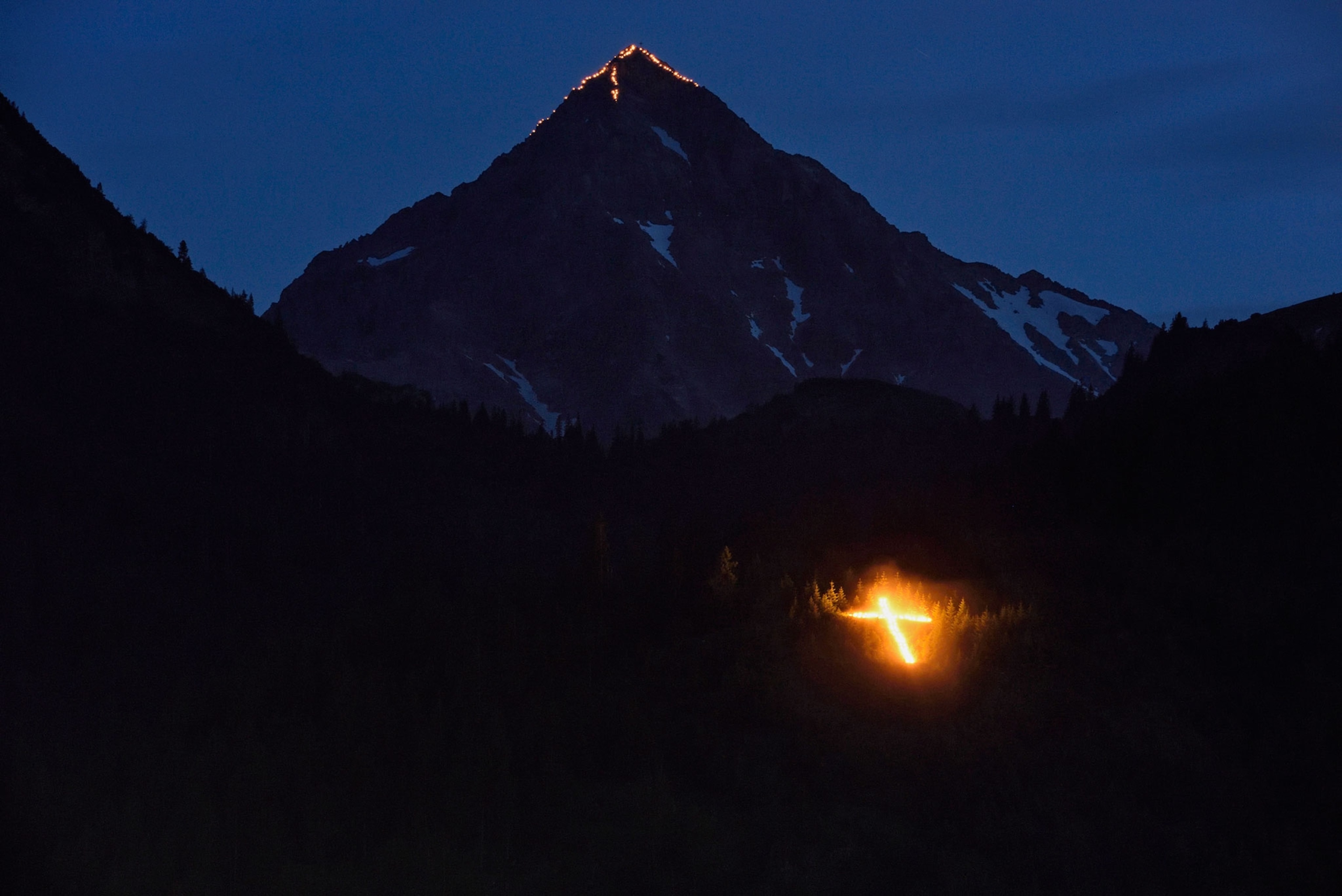 the peak of Geisshorn illuminated with bonfires along its summit ridges