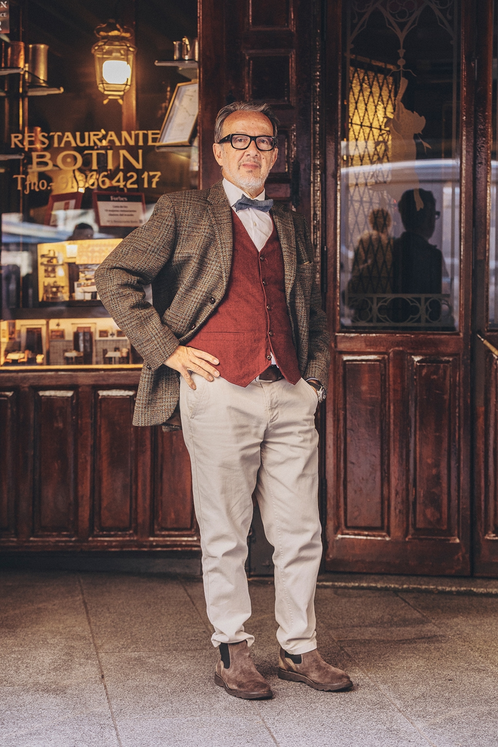 A dapper man in front of a wooden-panelled, old restaurant.