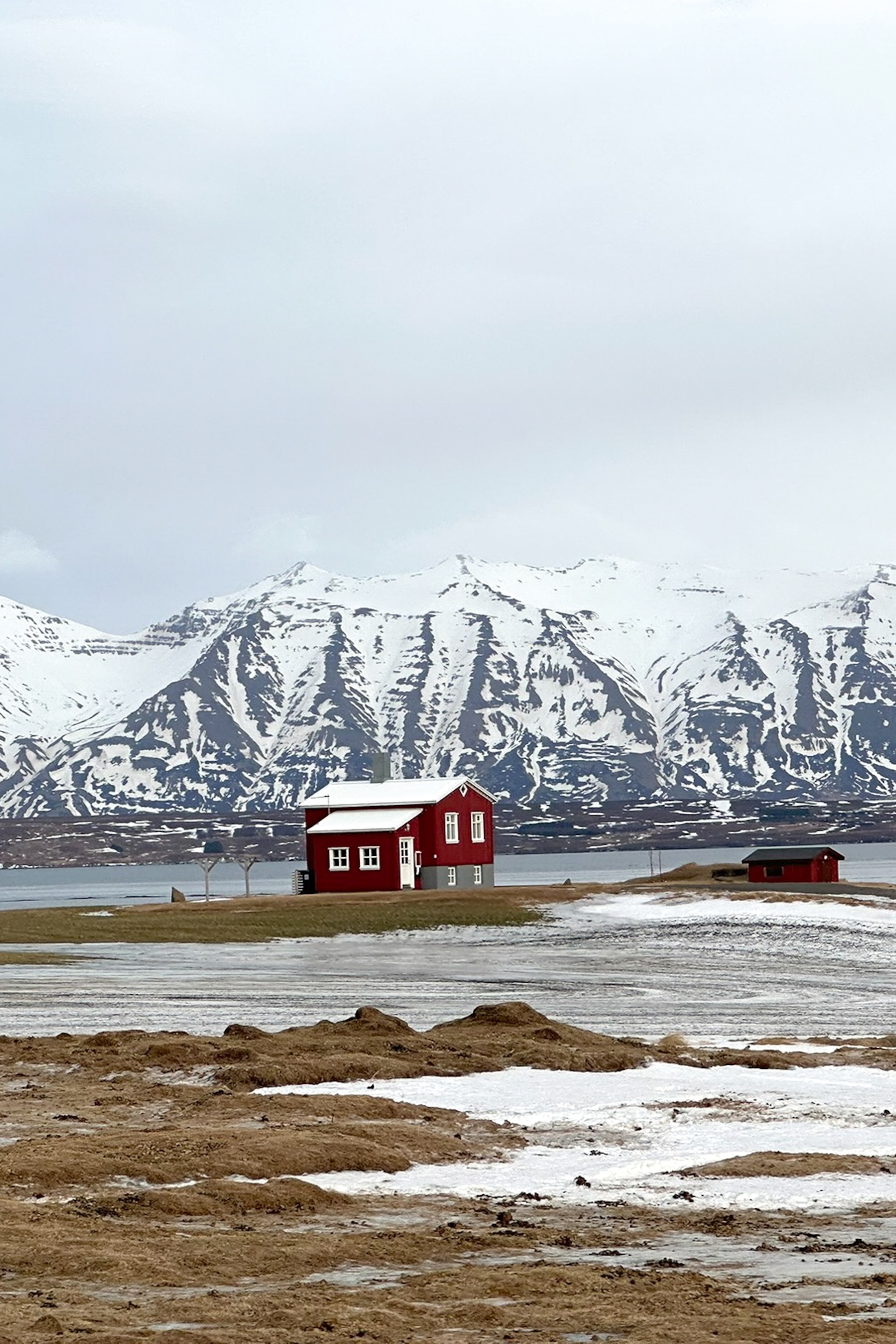 A sole block house built next to a river in a snow-covered landscape with mountains in the background.