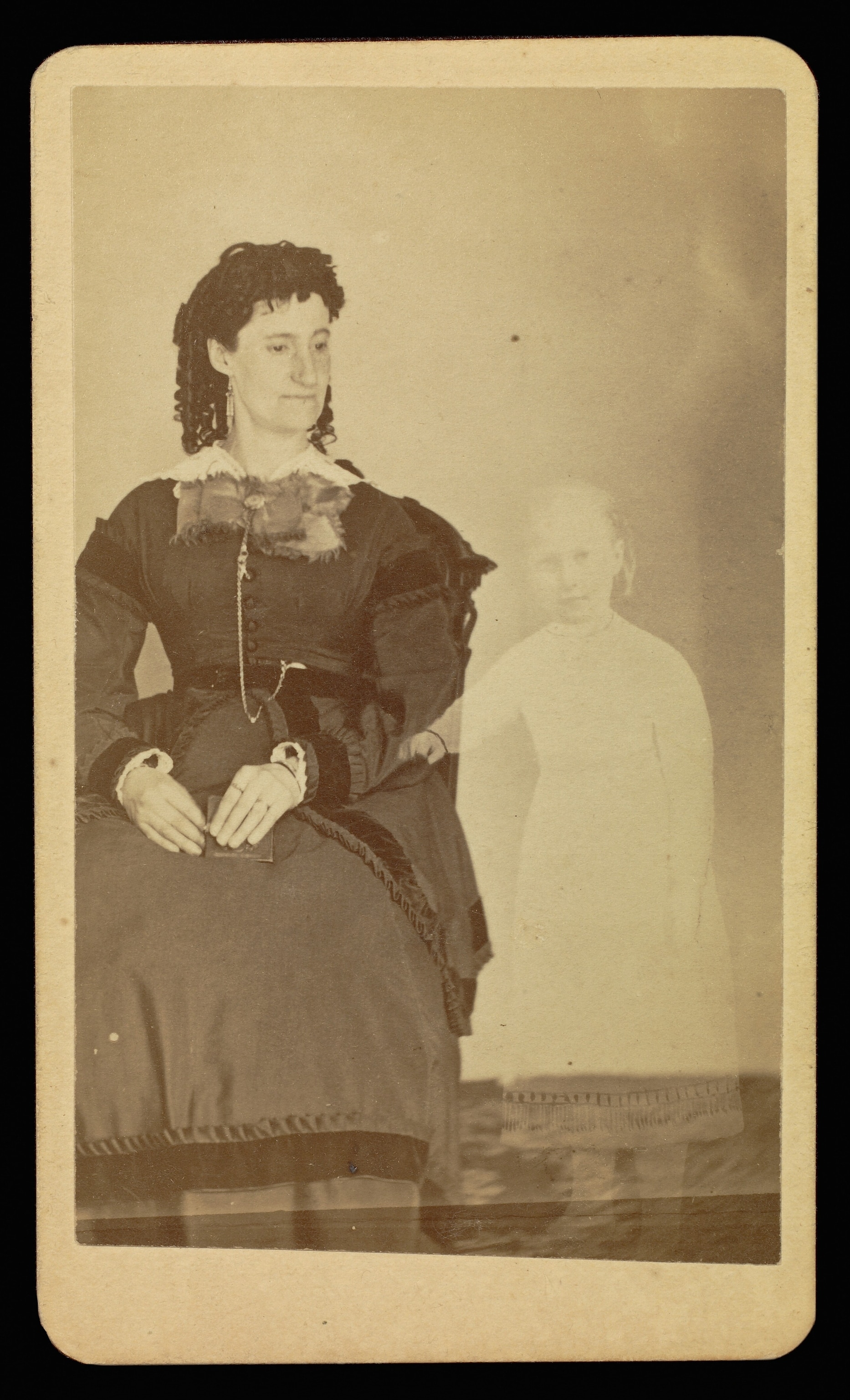 A figure of a child in all white, sat along stands along side a woman dressed in all black.
