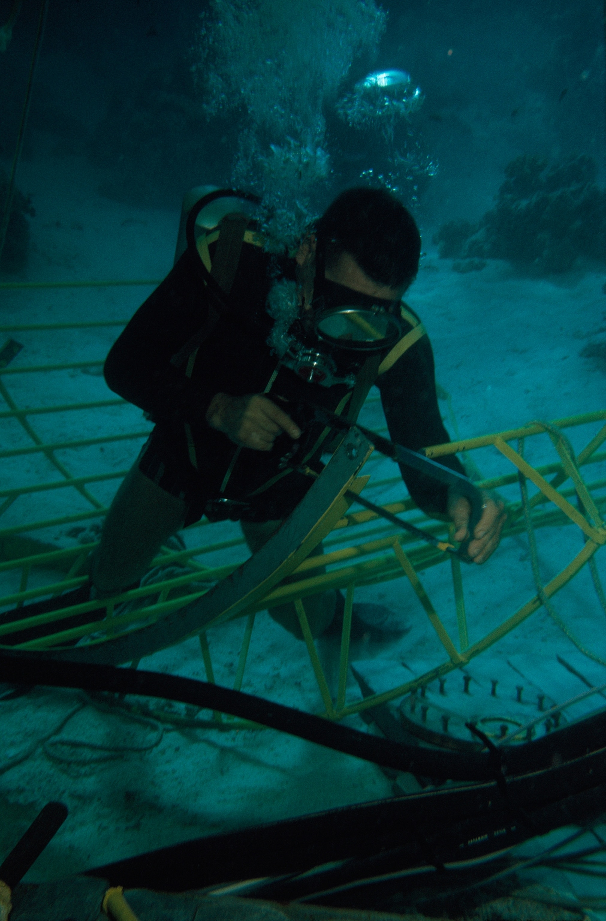 A diver uses a hacksaw to trim a metal rib of a sharkproof cage.