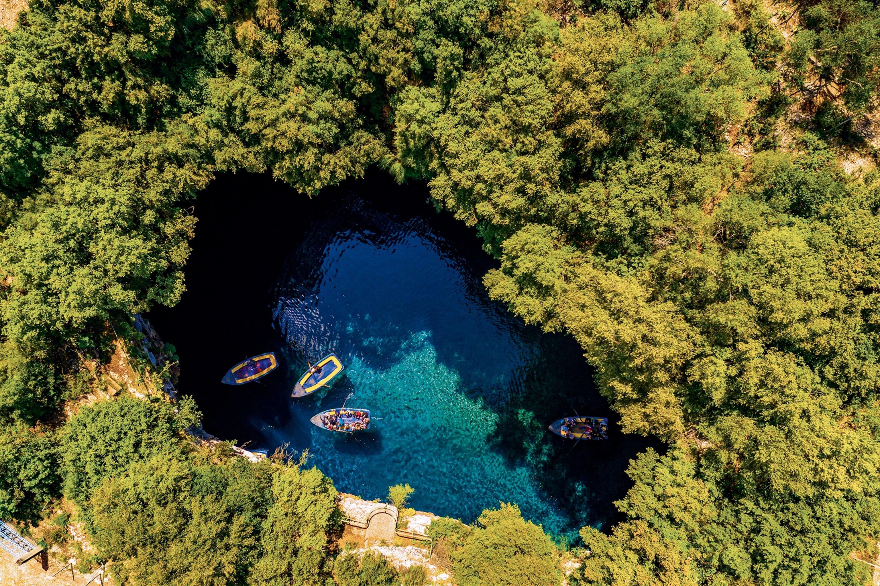 An aerial shot of an enclosed lake surrounded by thick vegetation with boats anchored in the middle.