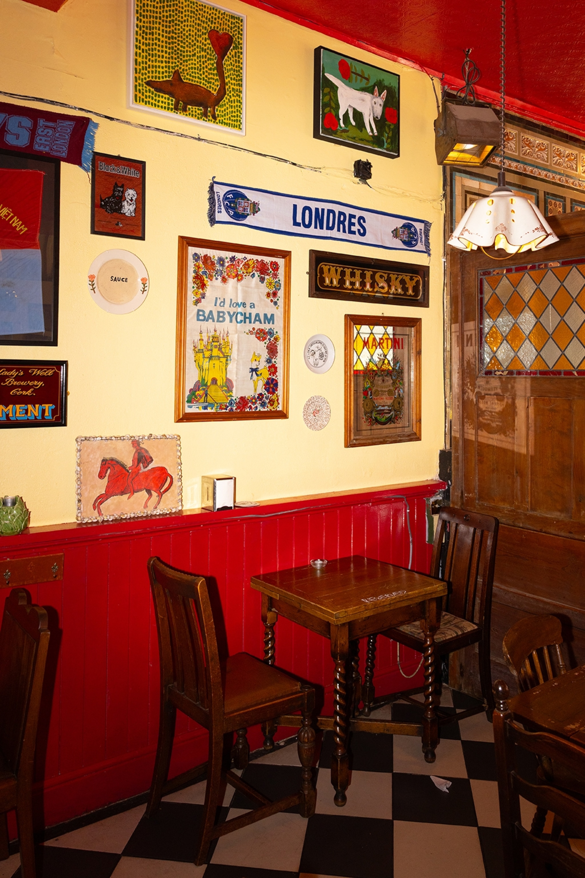 The indie interiors of a pub with a tiled floor, simple wooden chairs and Portuguese posters on the walls.