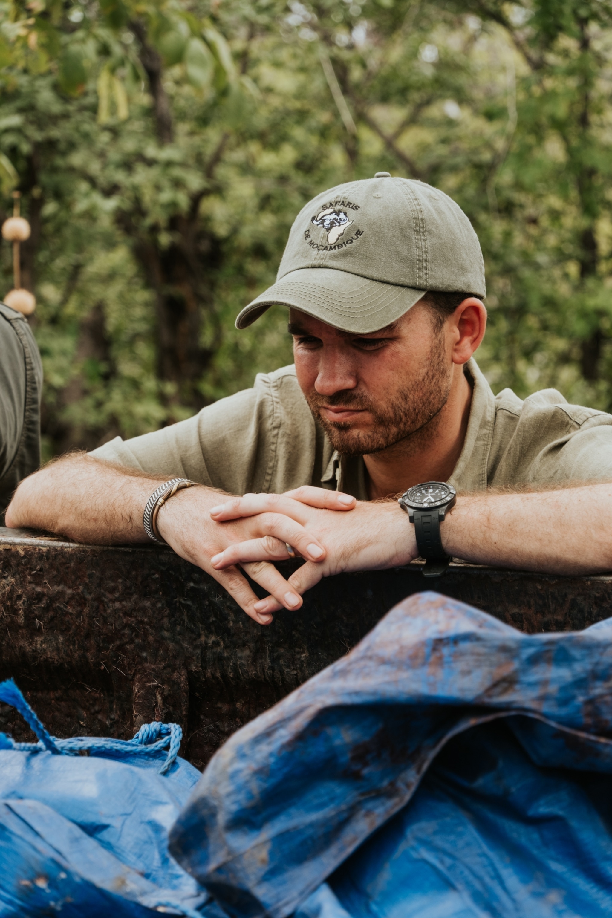 Man in green cap leaning on a rusty metal surface, with a contemplative expression.