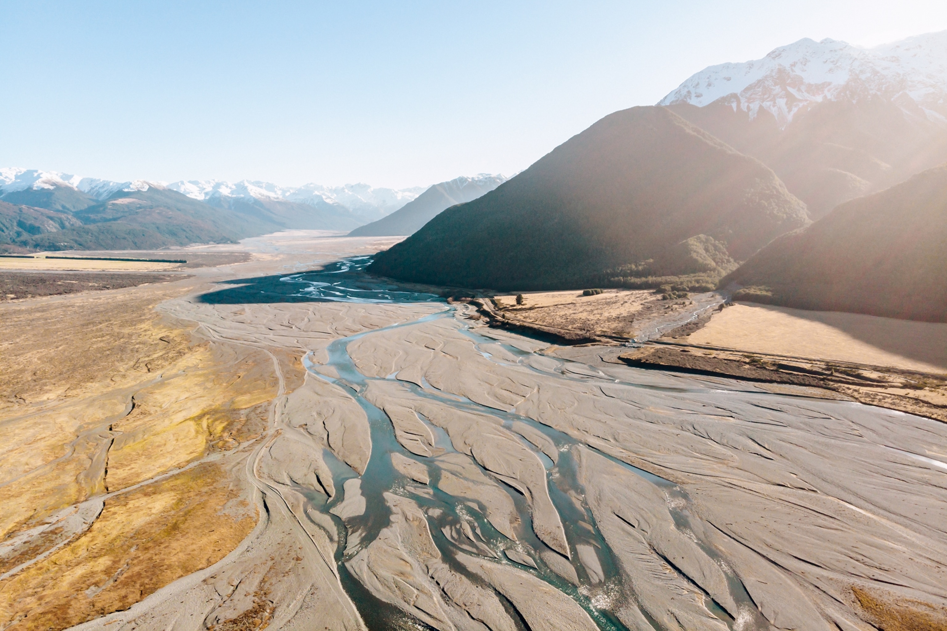 An aerial shot over a wide sandbank running through a mountain valley with the river broken up into hair-like strands.