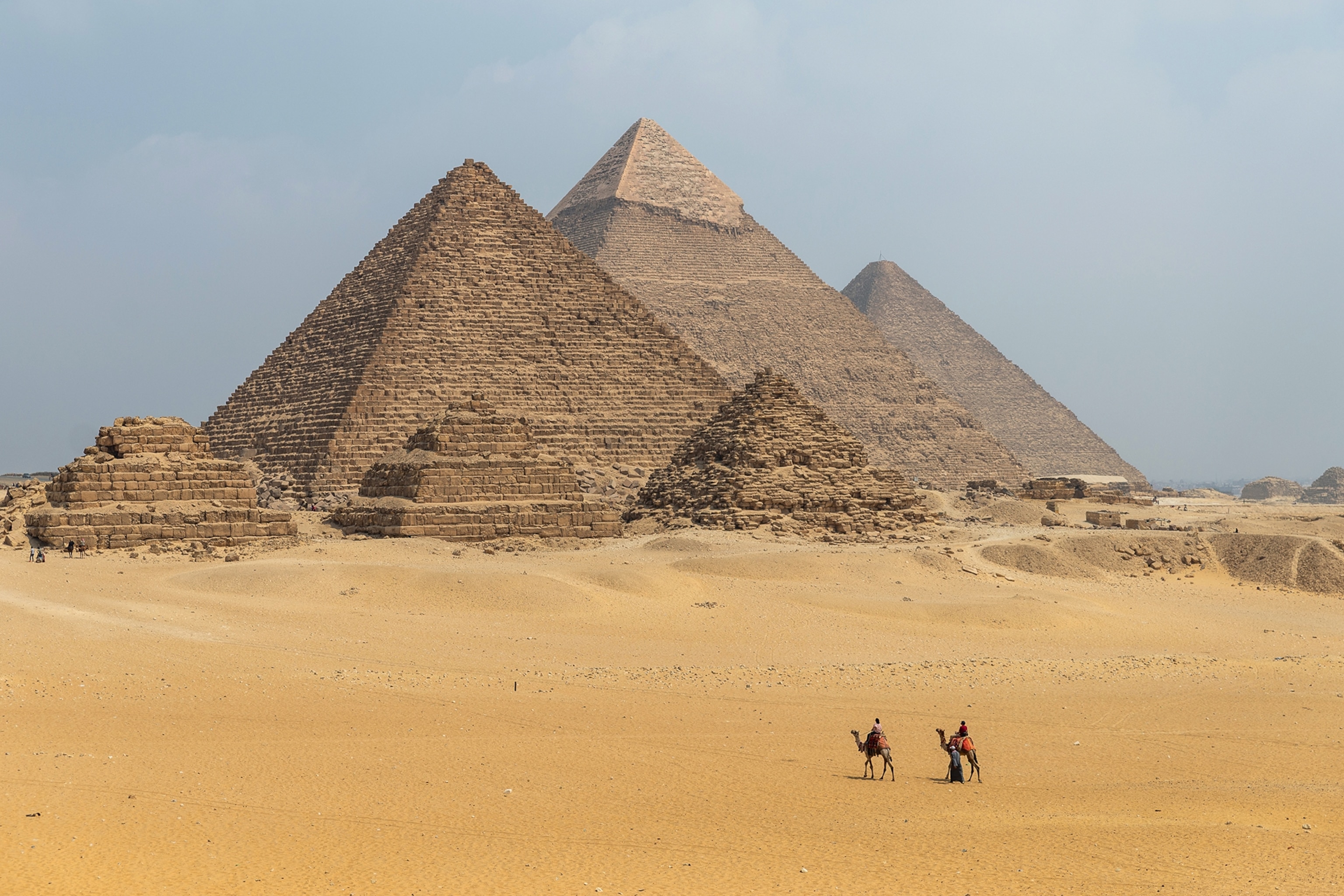 The pyramids of Giza with two camels passing in the front.