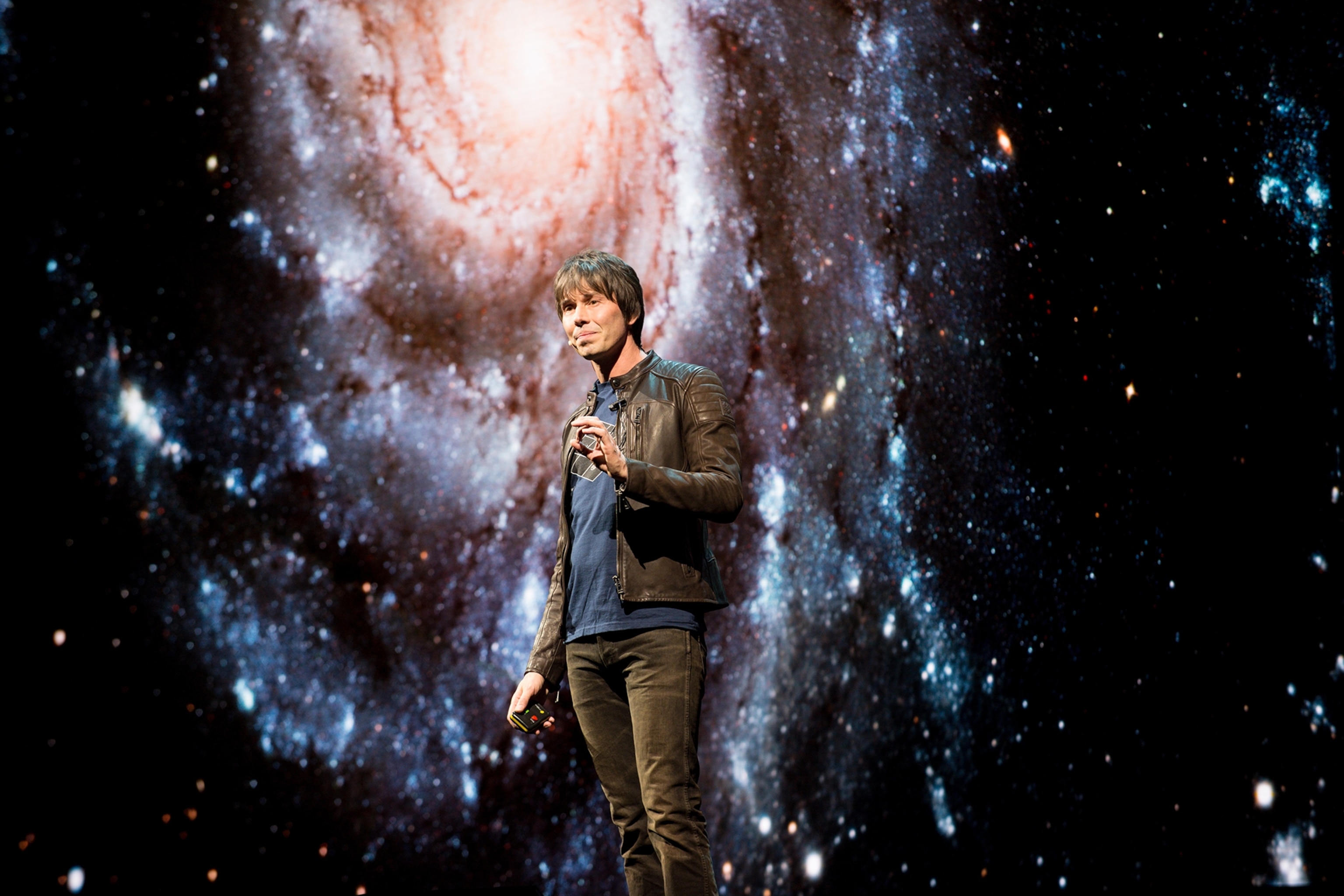Physicist Brian Cox presenting in front of a giant screen showing the Milky Way planetary system.