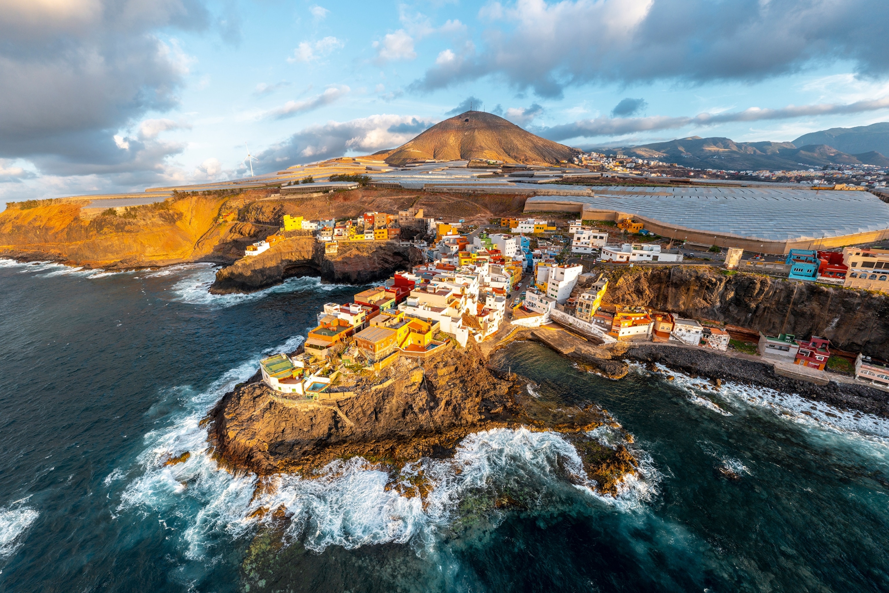 An aerial shot of a town set on the edge of cliffs as ocean waves crash onto the rocky shoreline below.