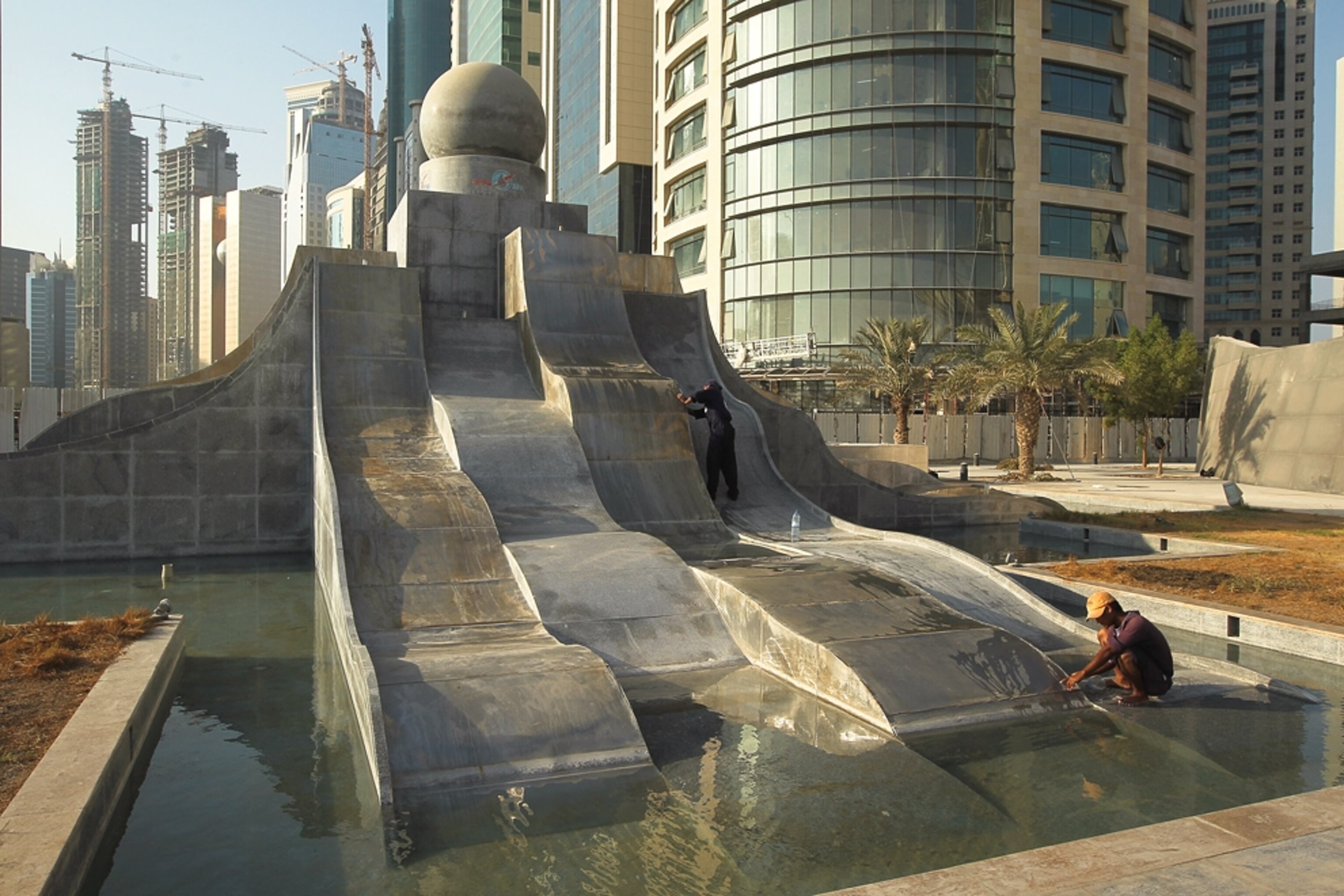 Workers clean a fountain amid skyscrapers in downtown Doha picture.