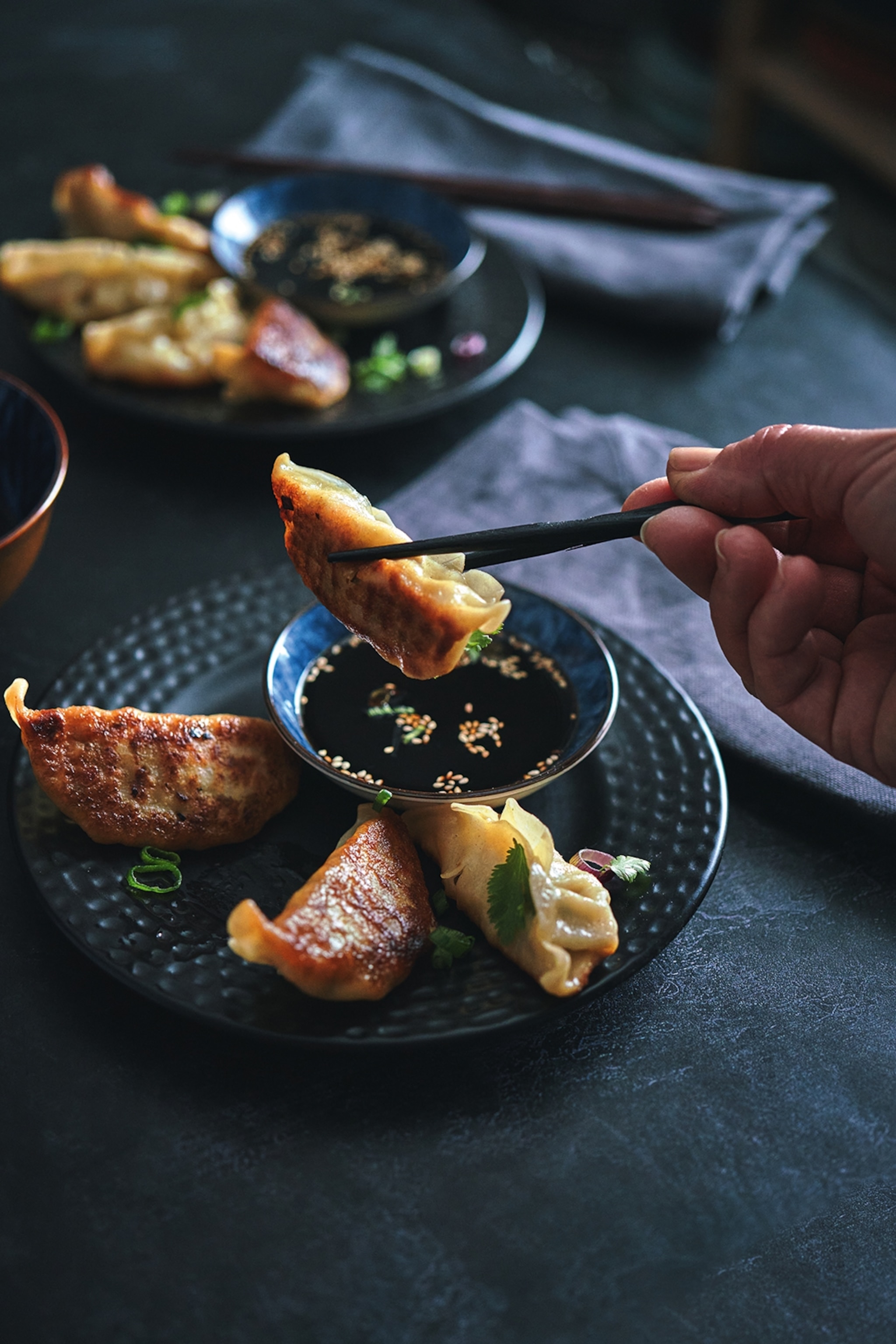 Gyoza dumplings being dipped into a dark sauce with chopsticks.