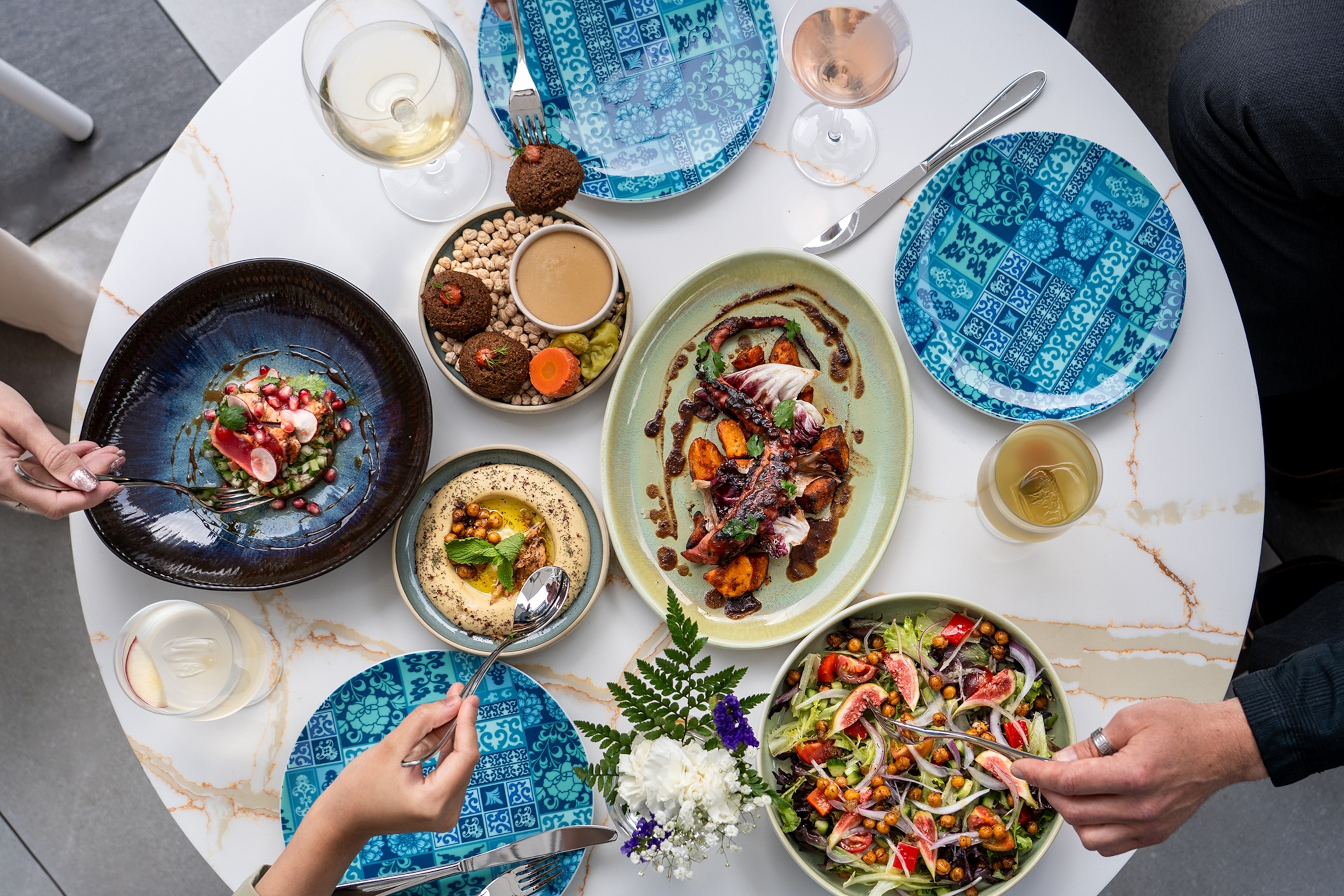 A marble table set with multiple plates of Eastern Mediterranean food, including hummus, falafel and a fig salad.