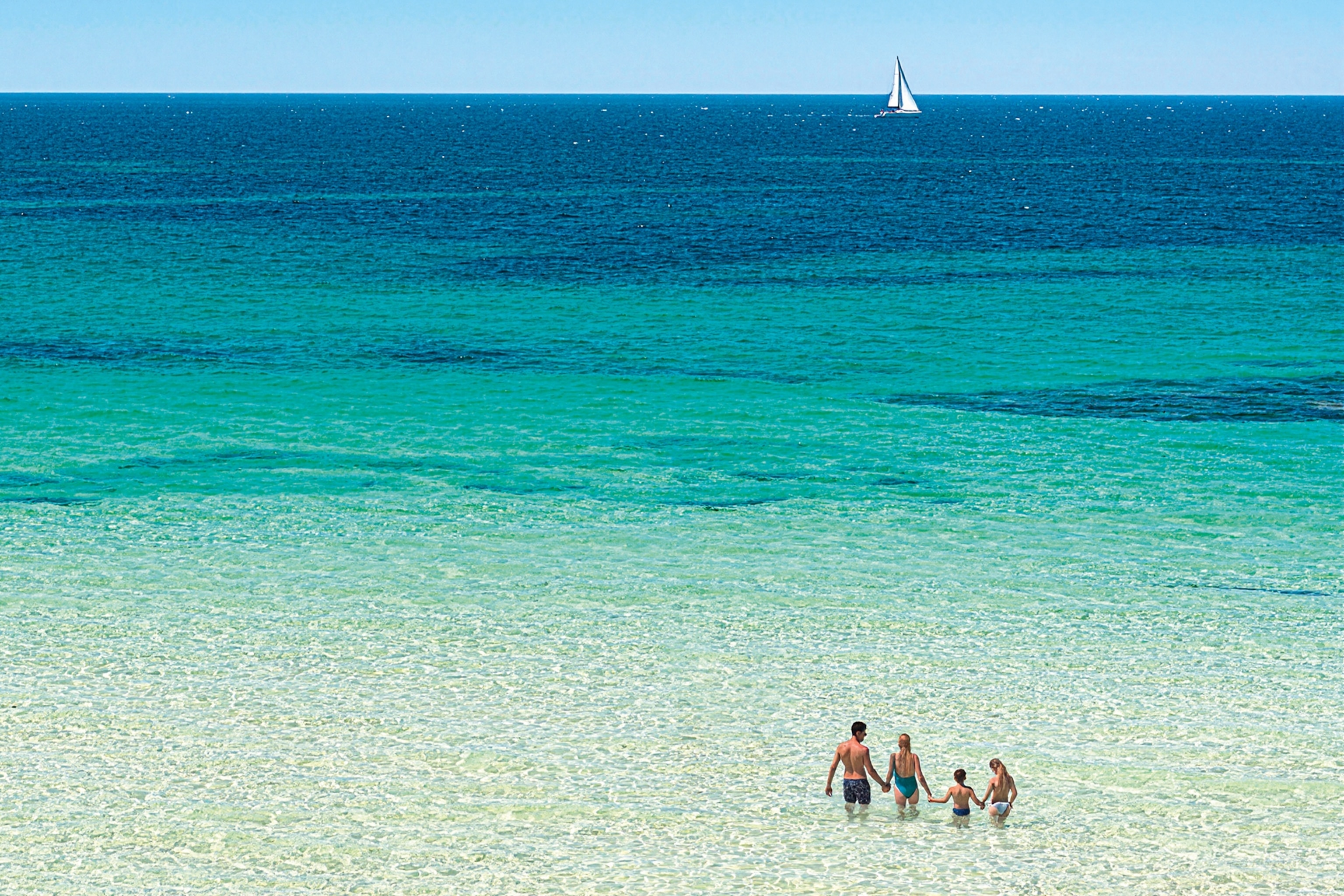 A beach with far-reaching shallow waters and a family standing in the front right hand corner in swimming wear.