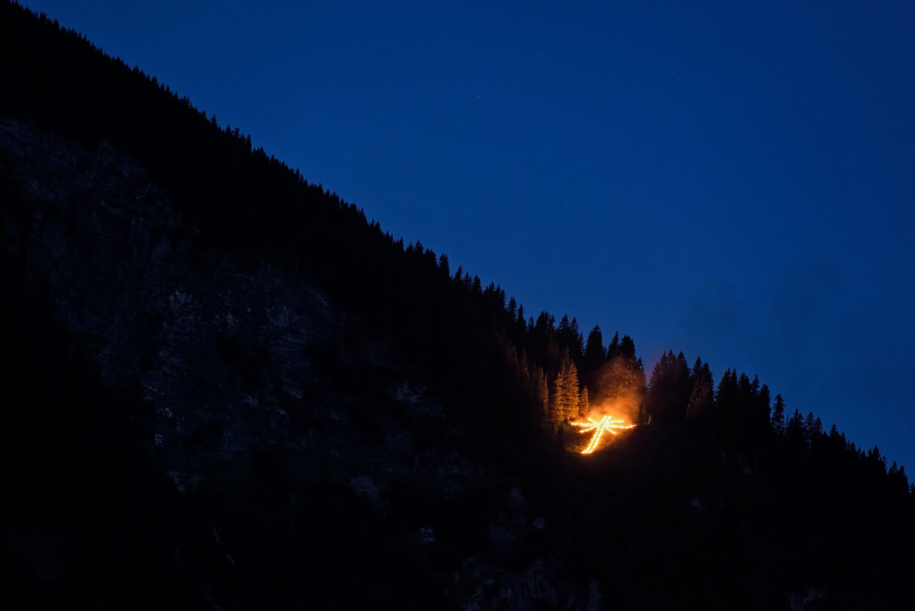 a cross lit by fire on the side of the Neunerkoepfle mountain