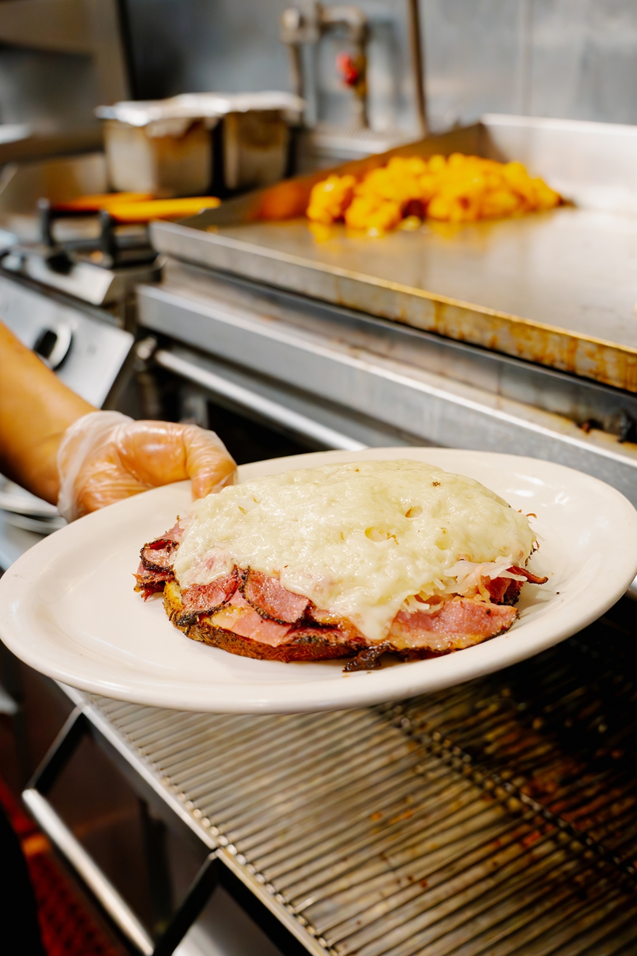 Someone holding up a plate of toast topped with layers of pastrami and melted cheese.