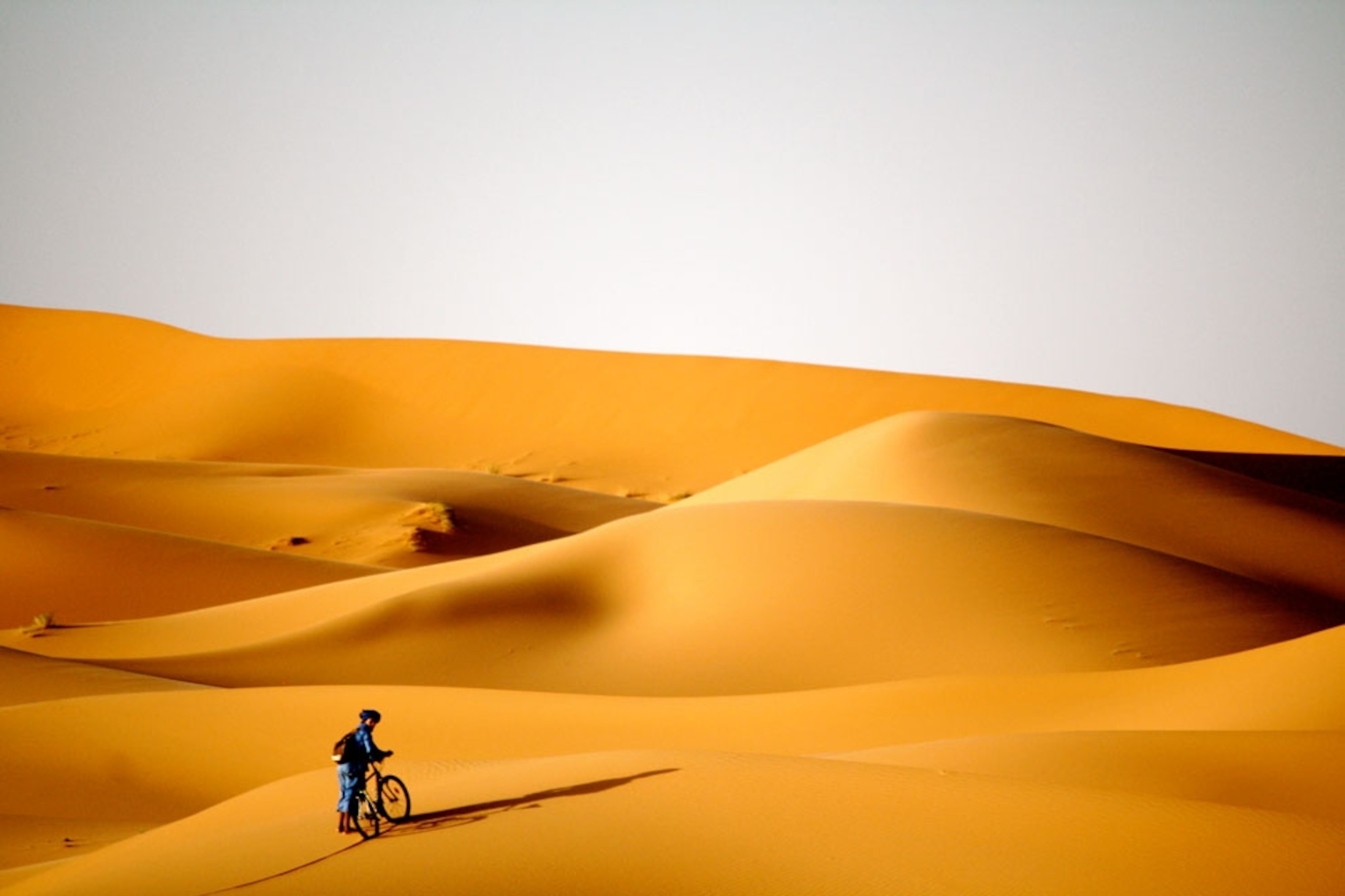 A man walking his bike along sand dunes in the Sahara Desert