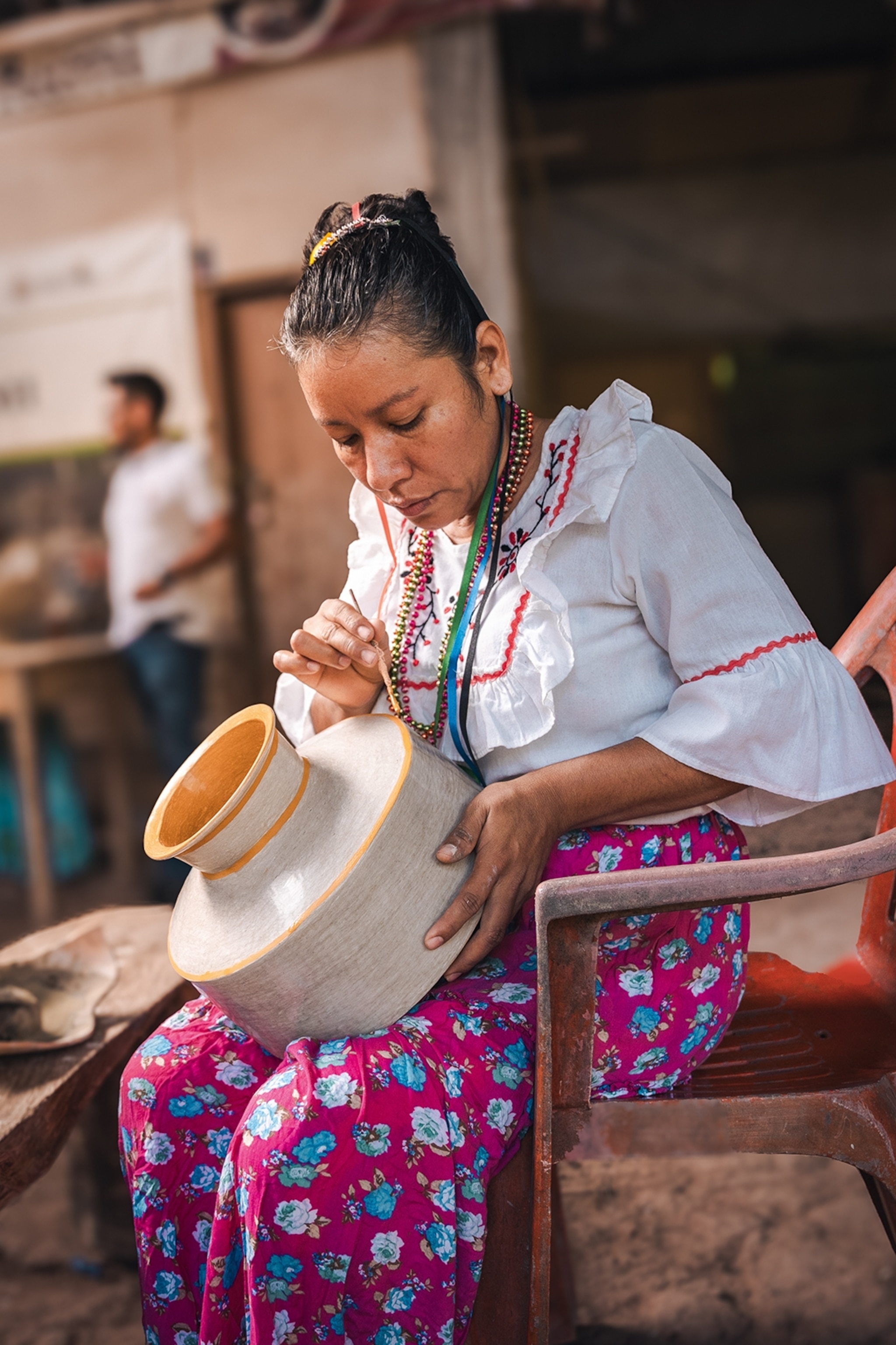 An young, indigenous woman painting a vase.