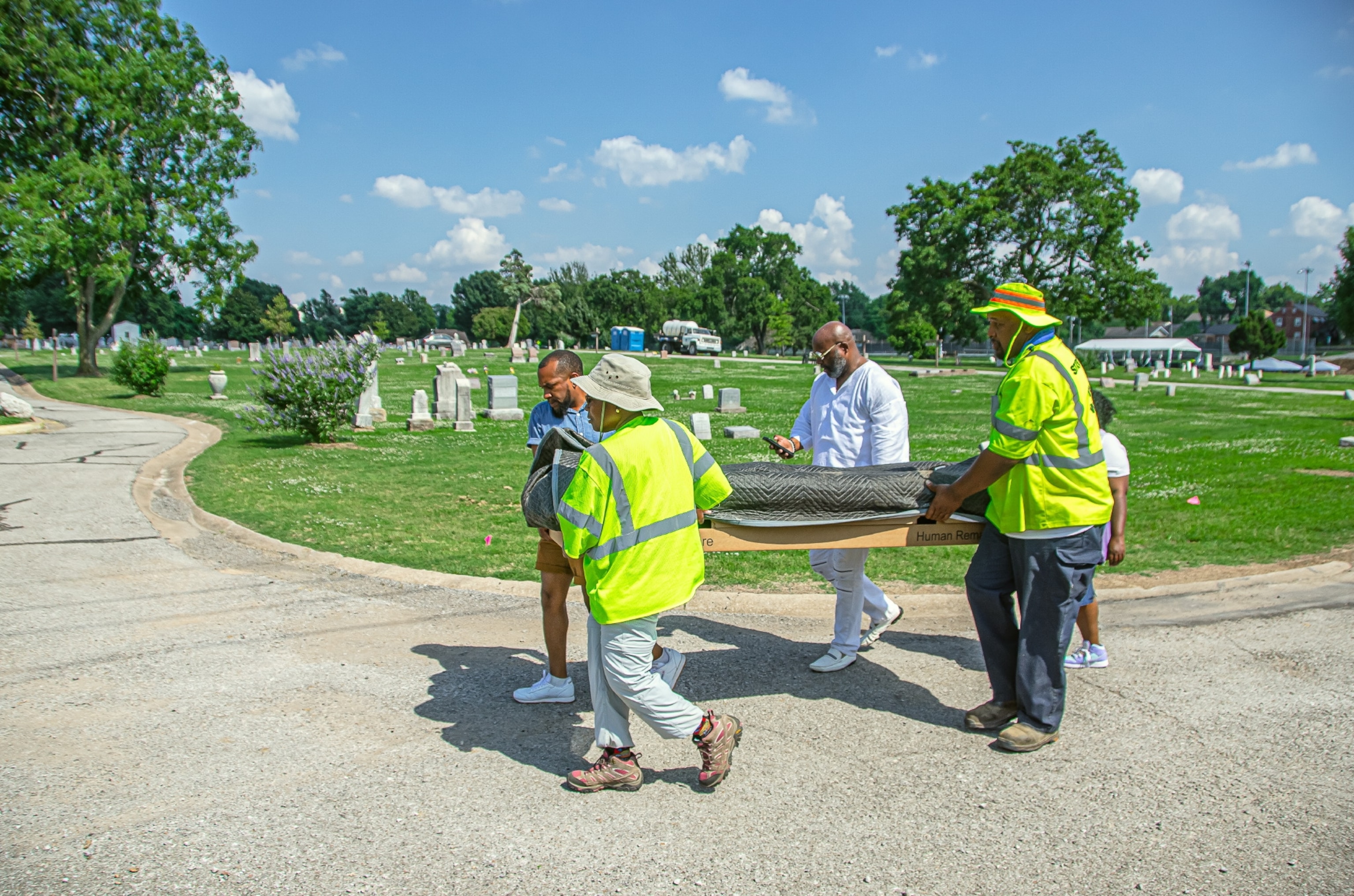 People carrying human remains covered with a black tarp through a cemetery