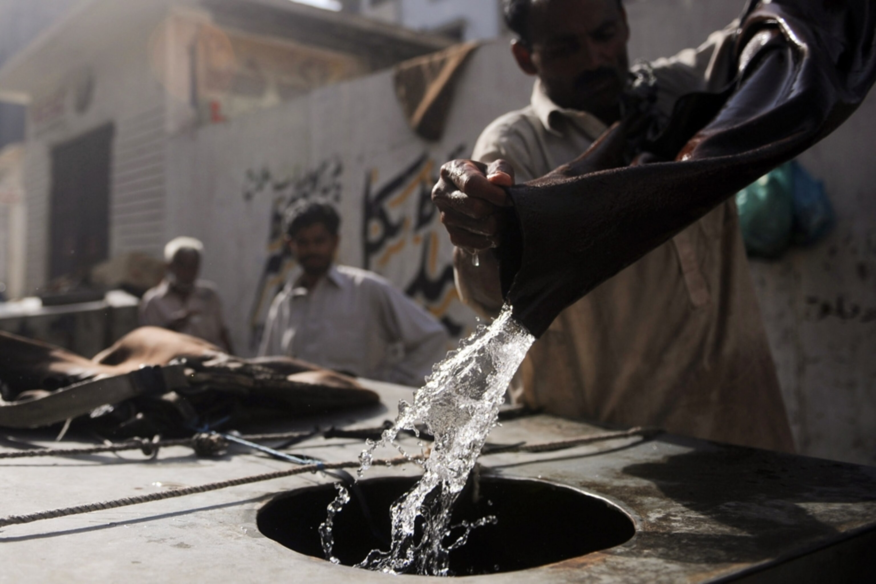 A Karachi water seller pours water from a leather pouch into a pushcart tank