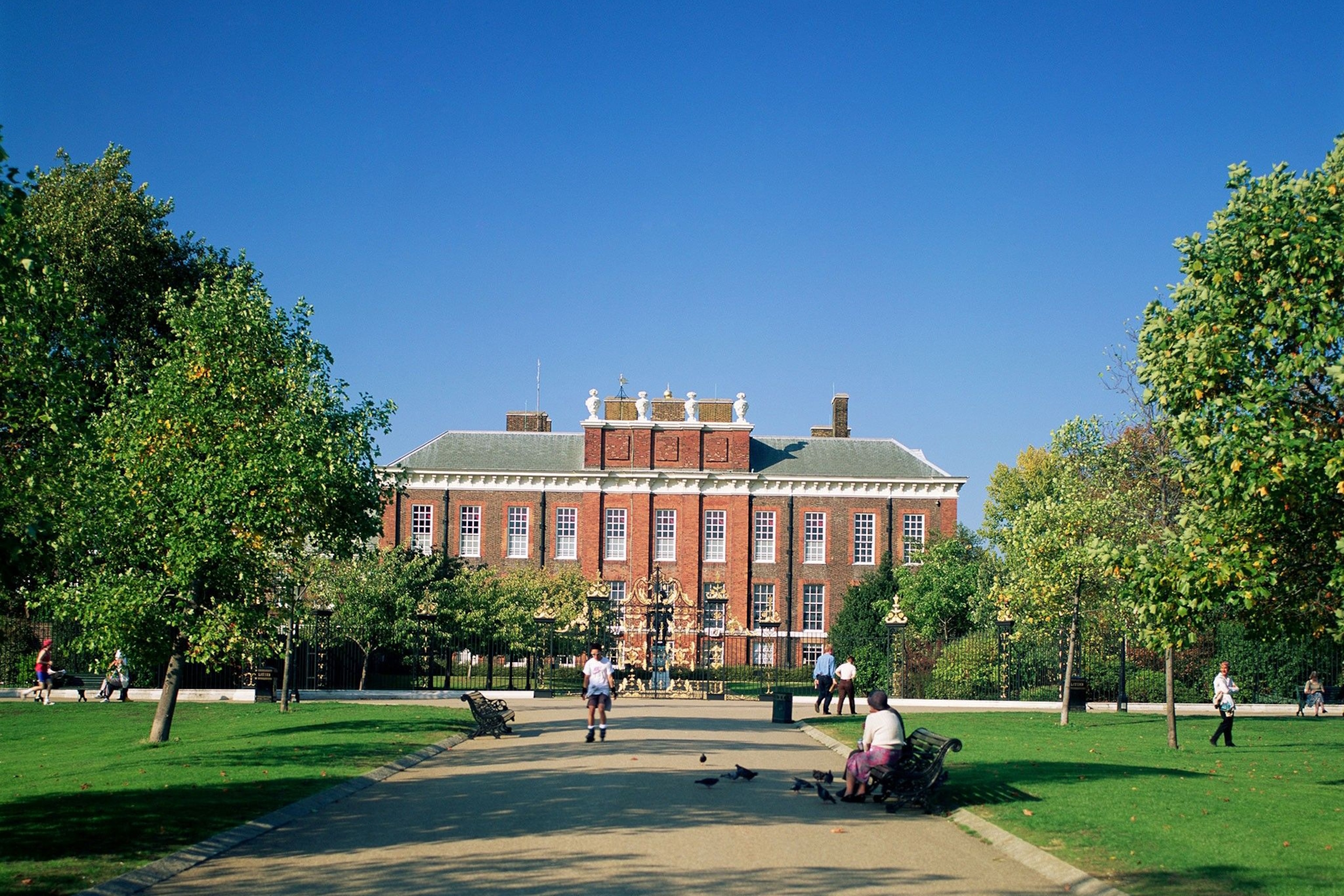 Front view of Kensington Palace with people sitting and walking through the grounds.