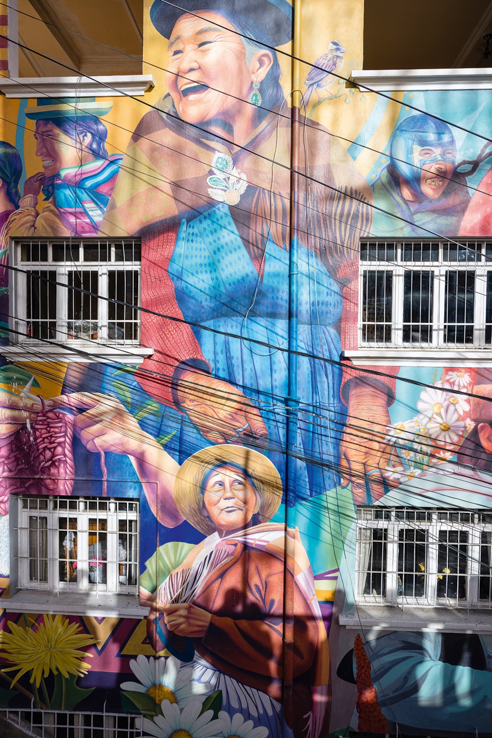 A tall mural on the side of a house in a mountain city, depicting Indigenous women.
