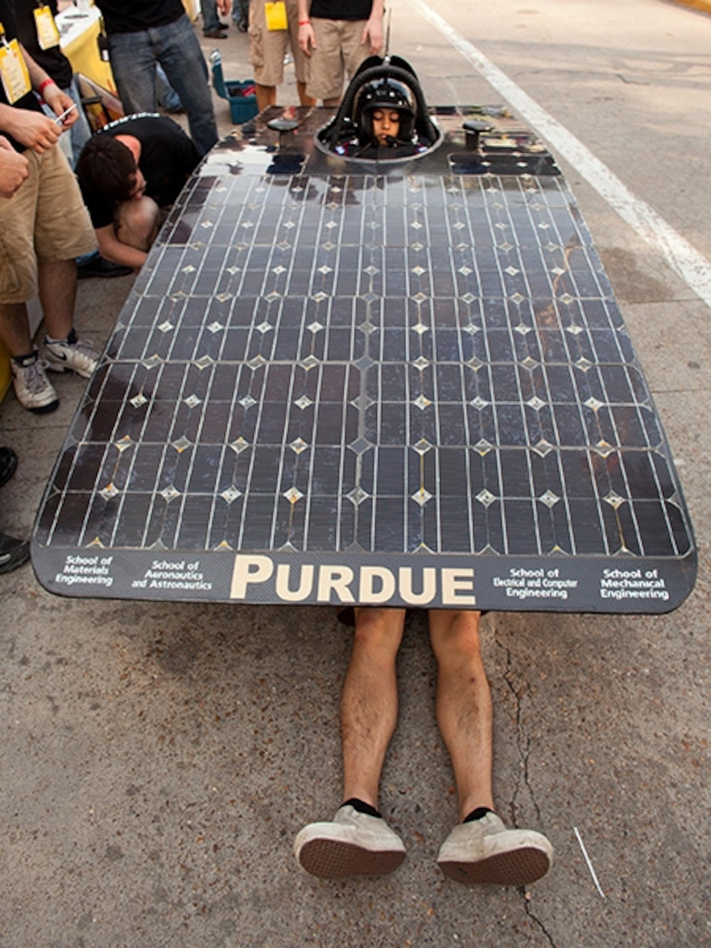 Purdue team member Kevin Wang works under the solar-panel body of the school's prototype entry while driver Sirisha Bandla waits to start a Sunday morning run.