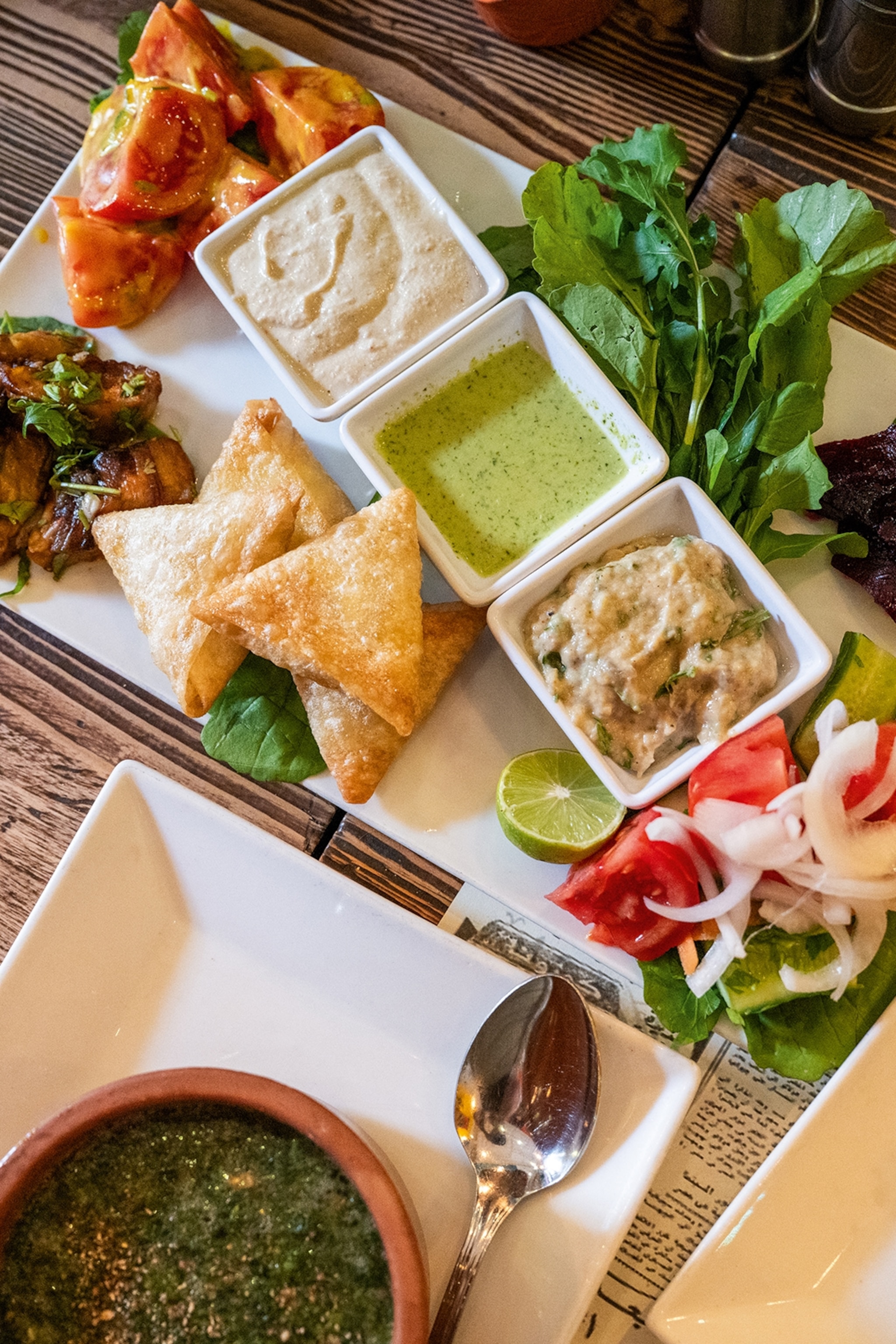 A plate with samosa-style pastries, sides and three sauces.