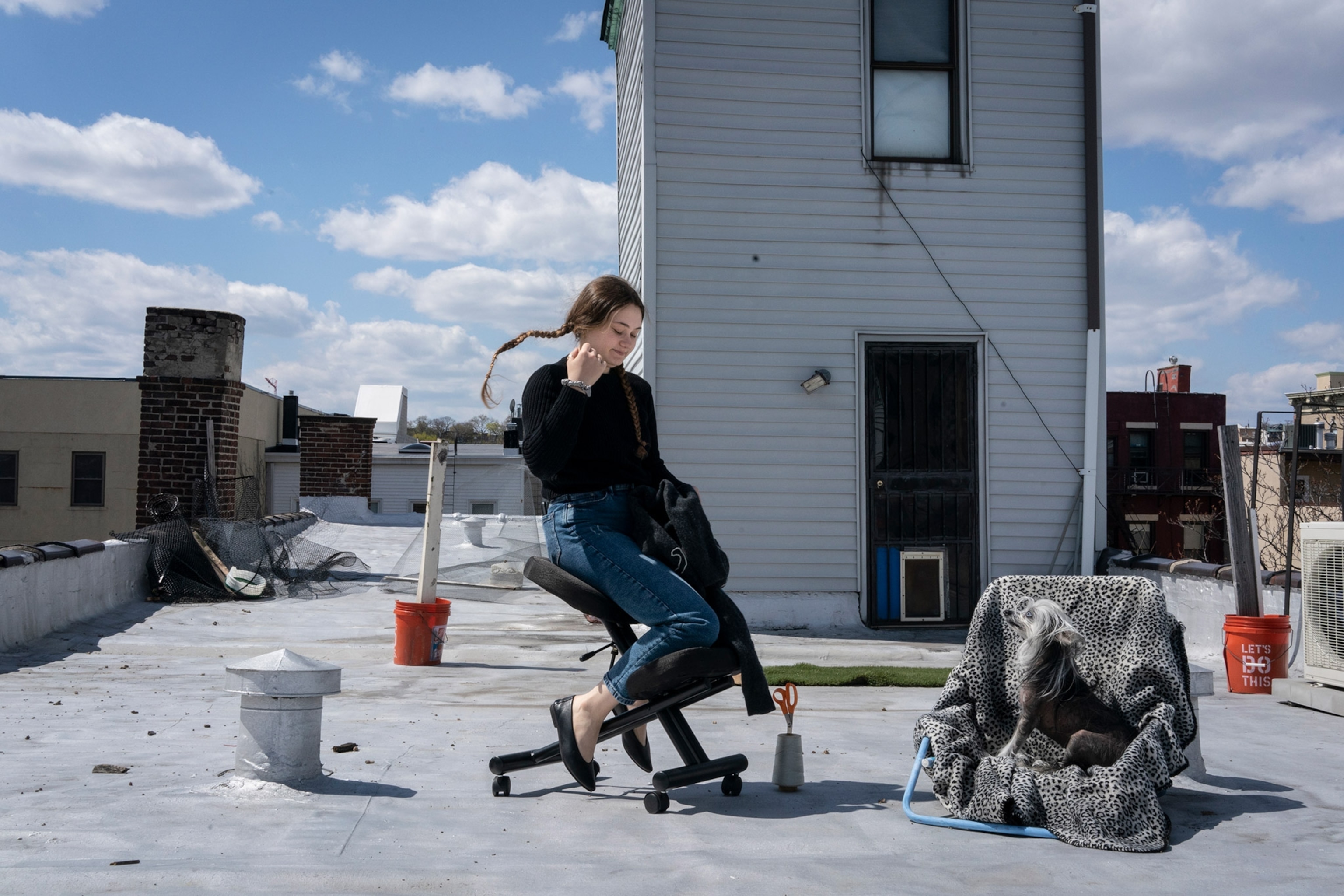 a girl on a rooftop sitting in a chair next to her dog