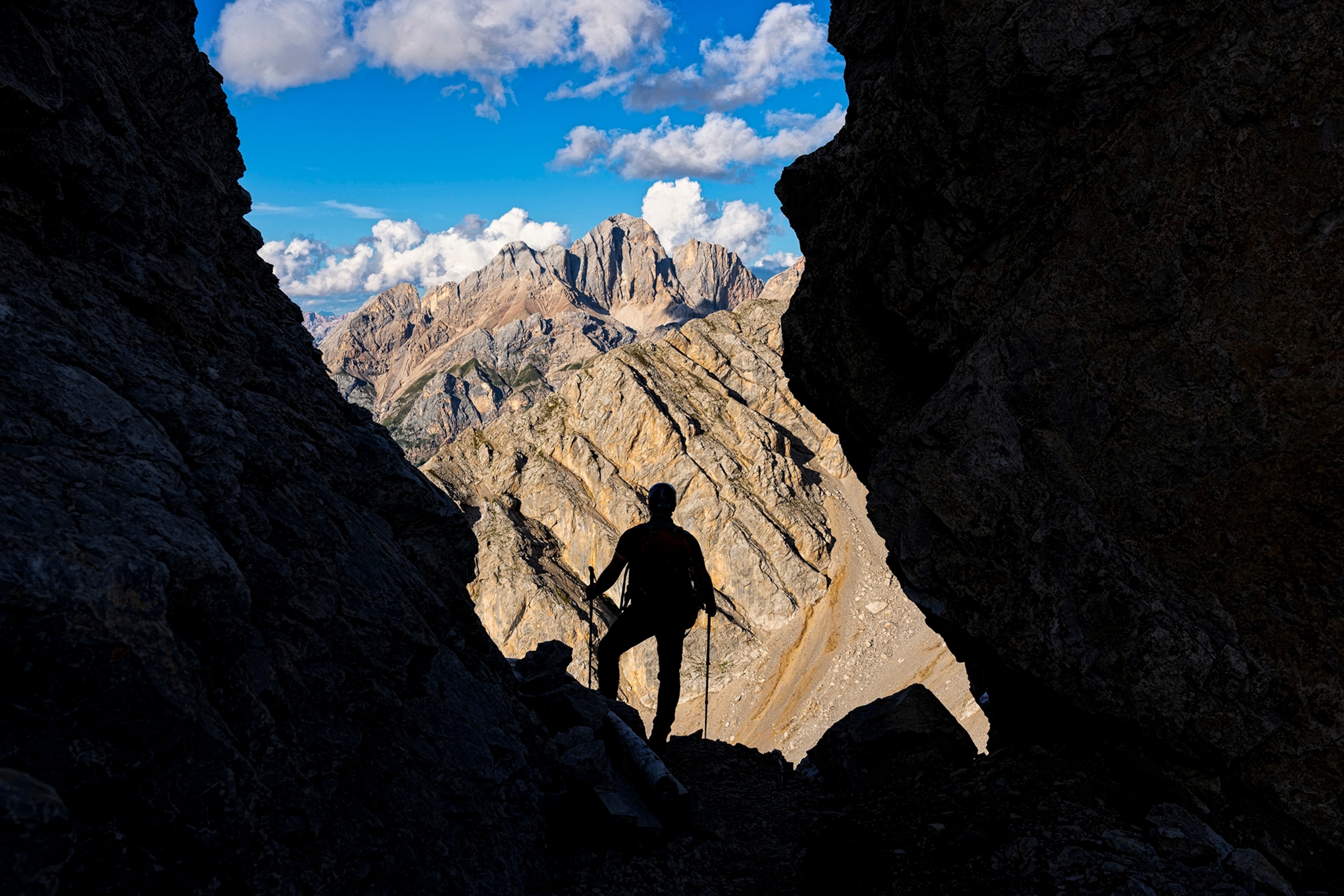 A hiker resting at the opening of a mountain cave, shot from the inside out.
