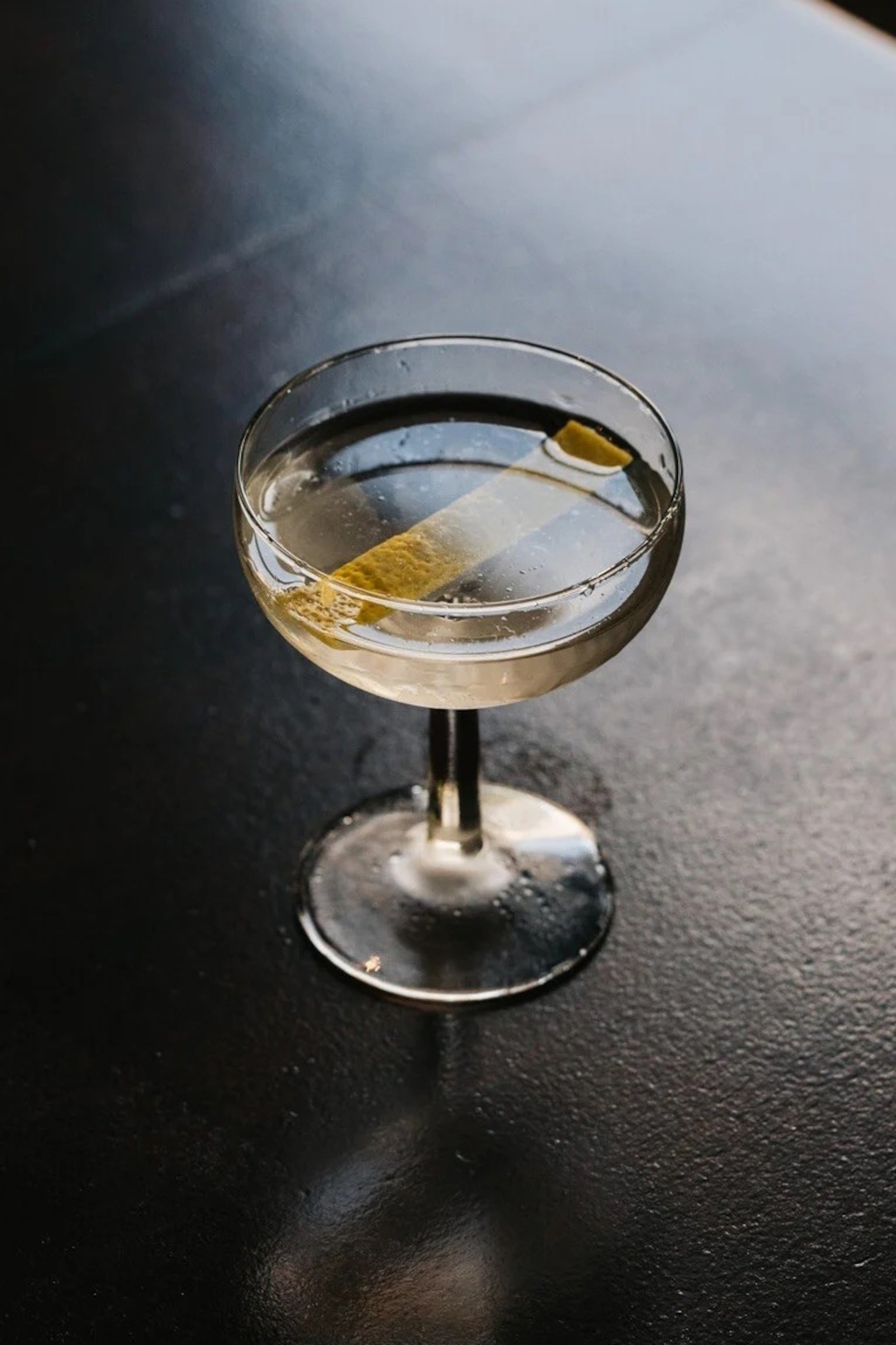A close-up of a clear martini in a small coop with a sliver of lemon rind.