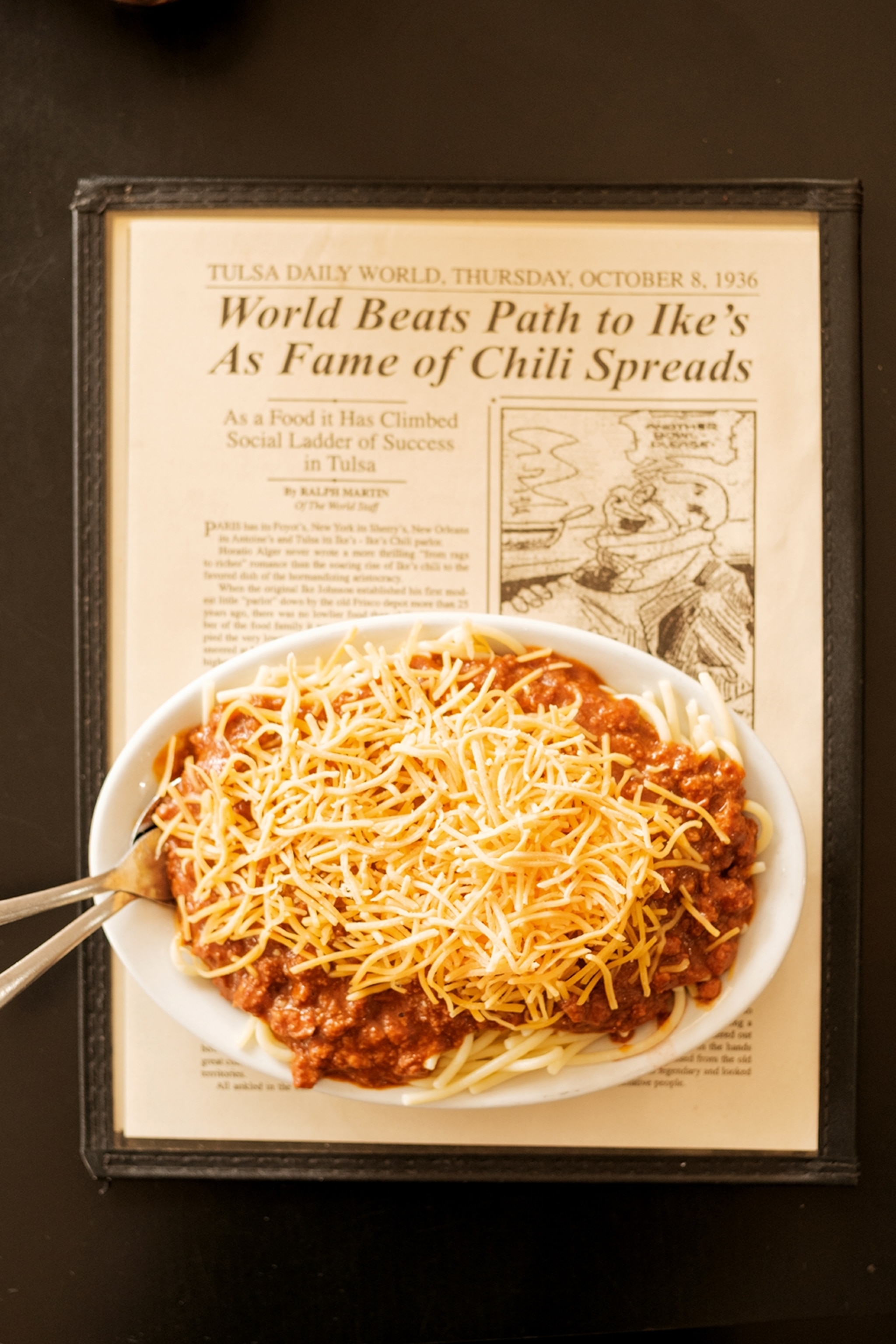 A bowl of chilli with spaghetti and cheese on top of an old, laminated diner menu.