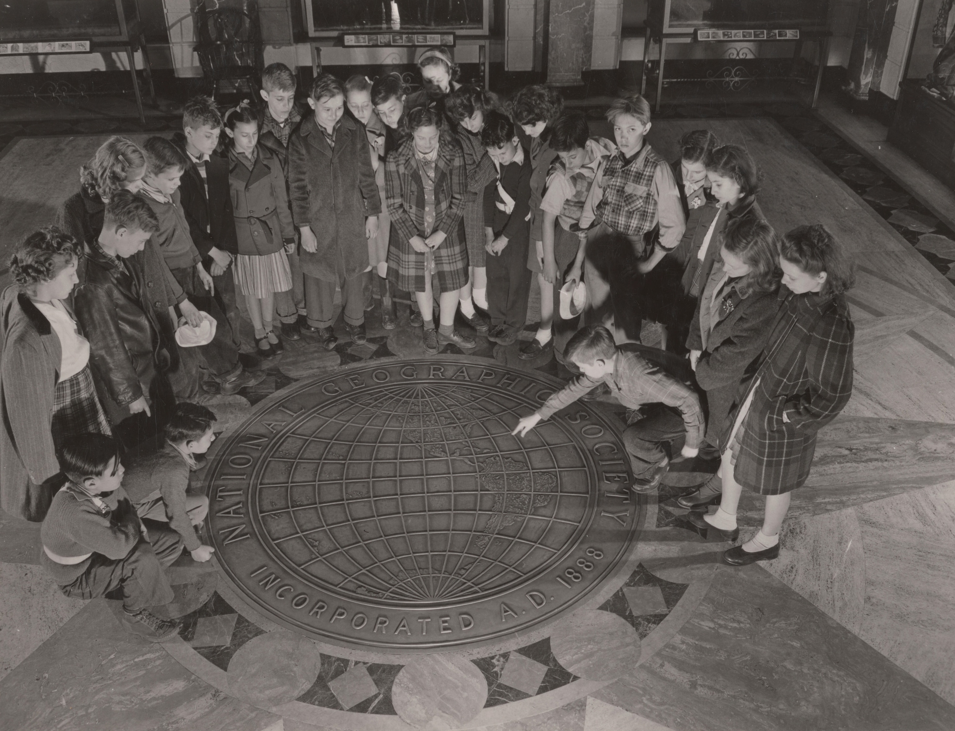 A group of children gathered around a circular flood inlay of a globe