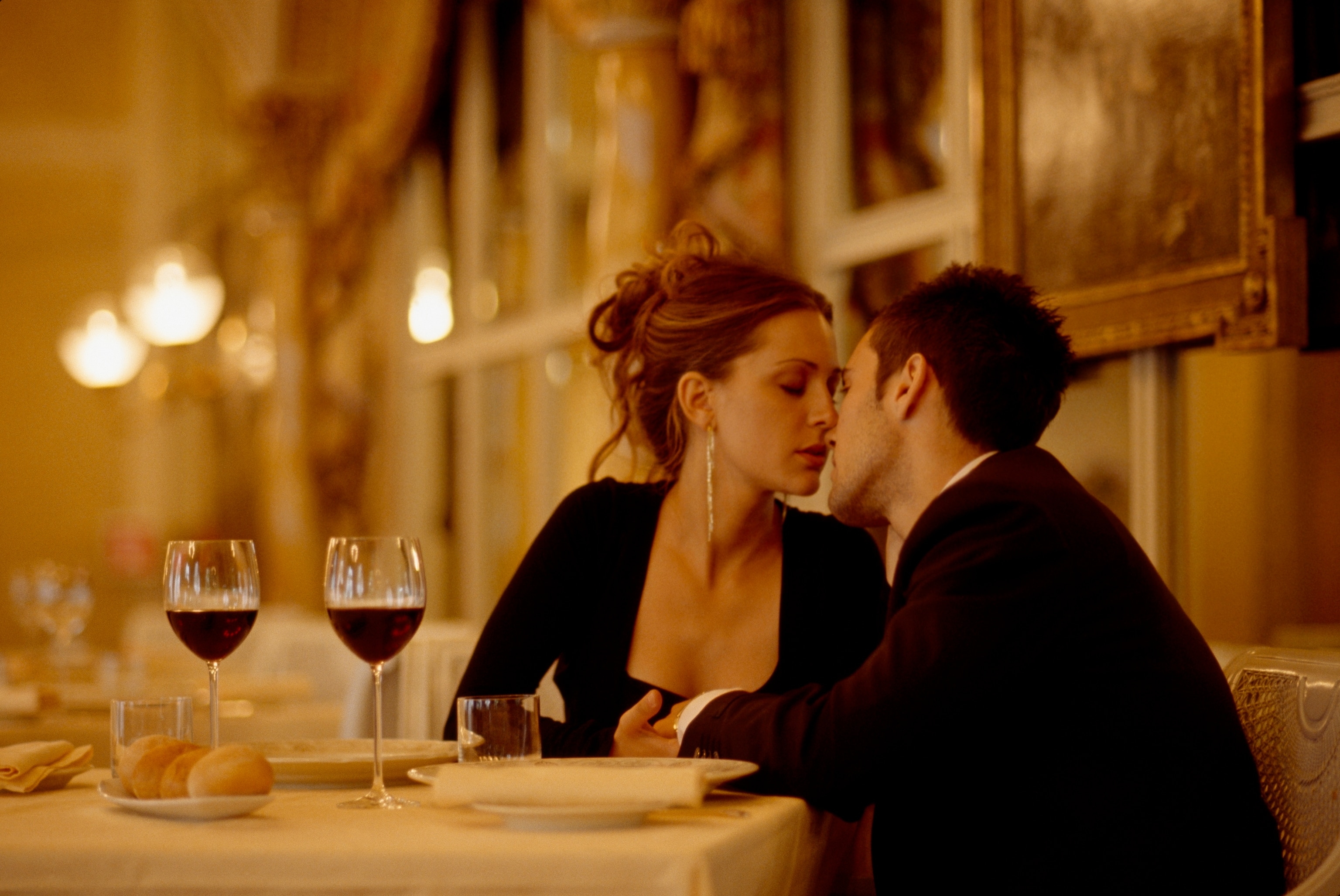 A couple holding hands and kissing at a restaurant table.