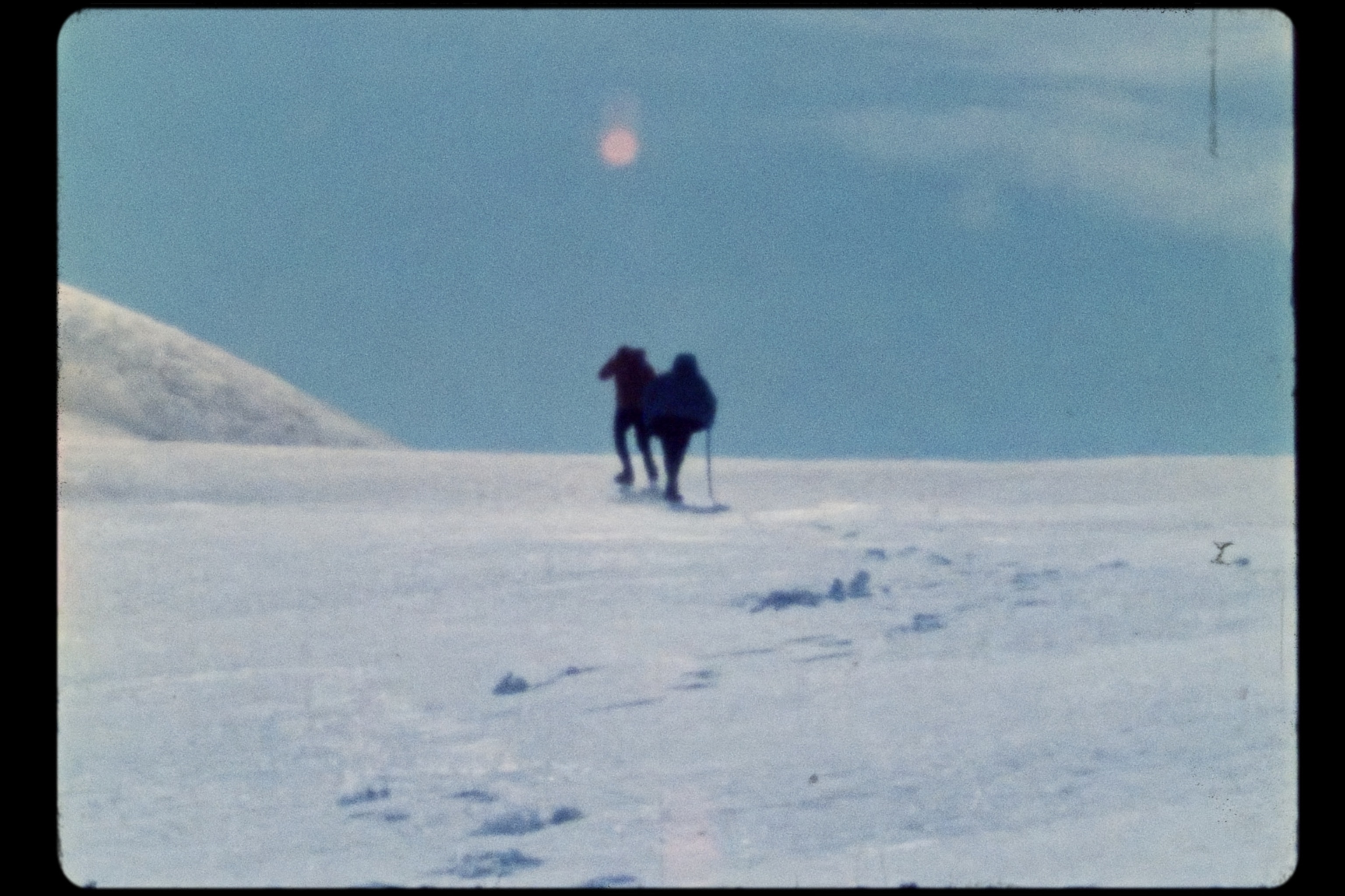 Two people hike up slope in glacier