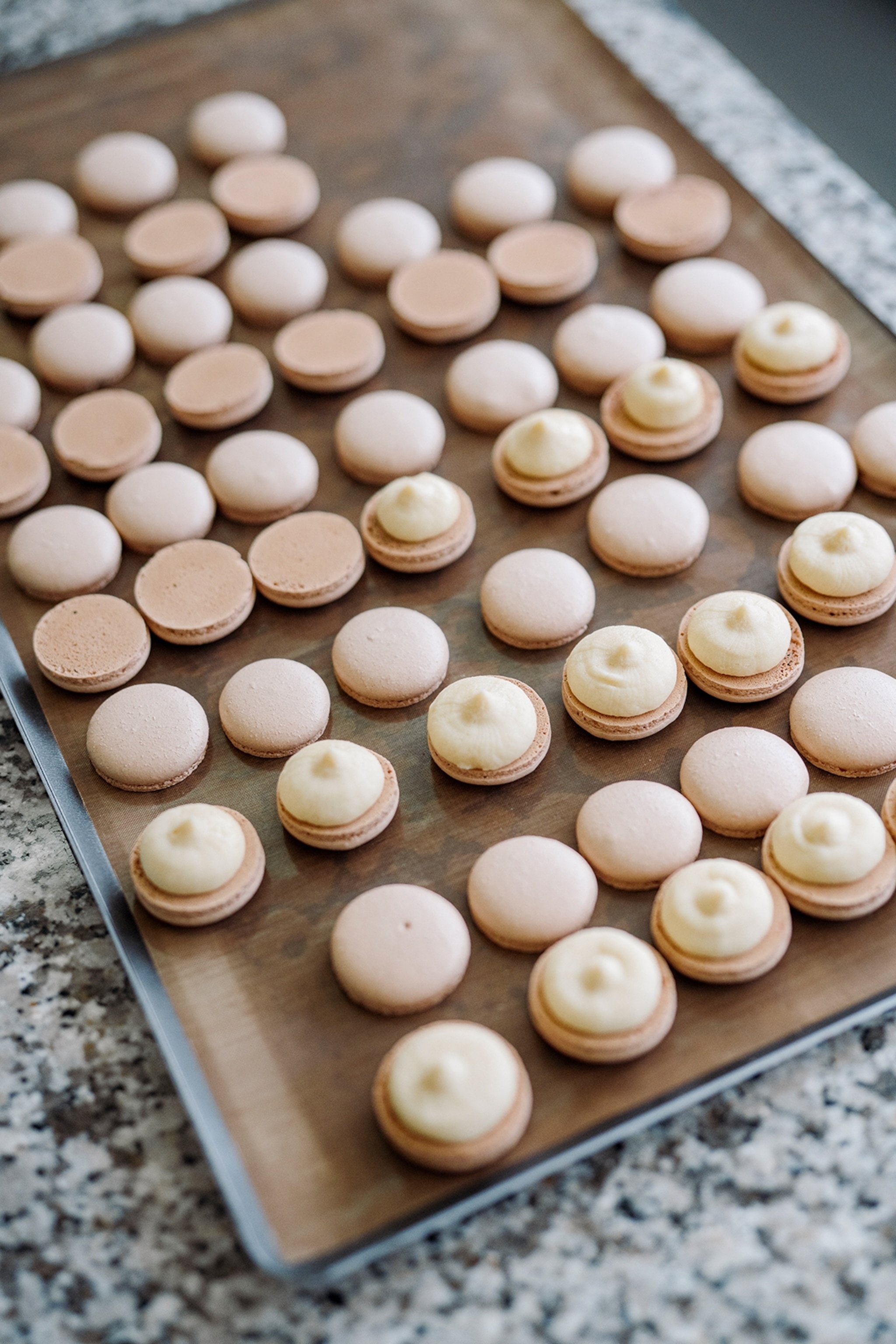 A close-up of a baking tray with macarons, both with filling and without.
