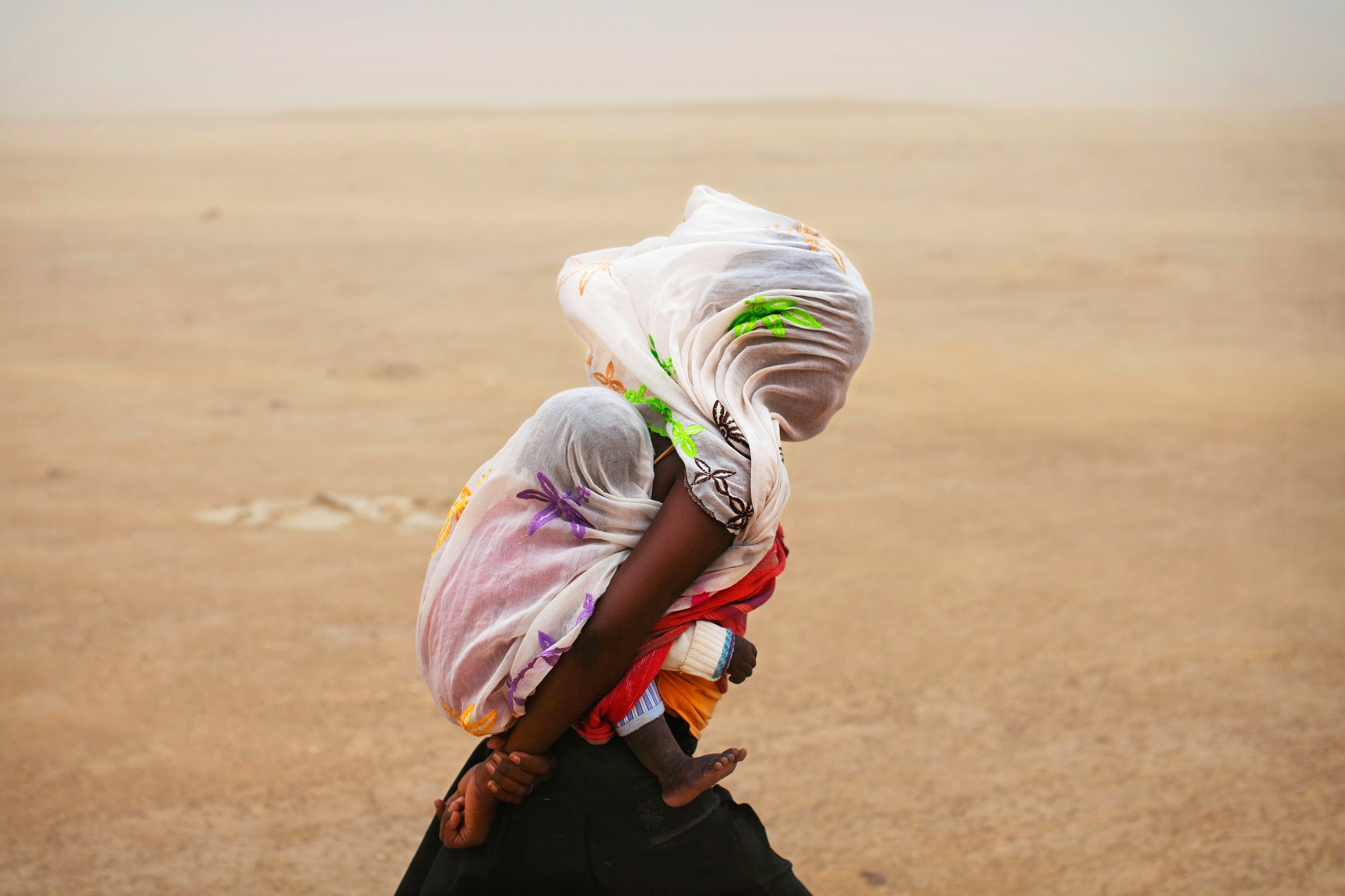 a woman carrying her baby through a sandstorm in Timbuktu, Mali.