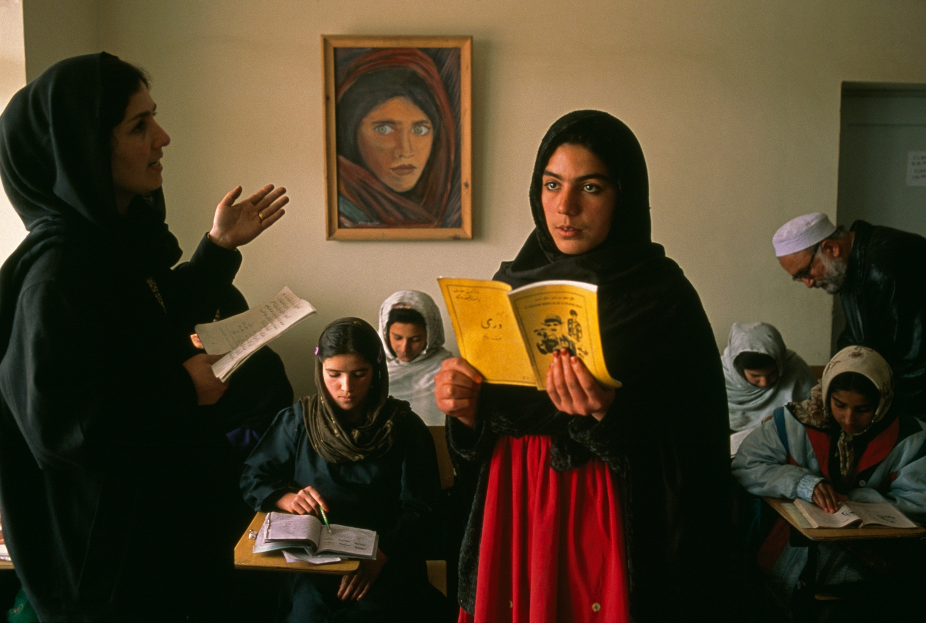 An Afghan girl reads from a booklet in a classroom.