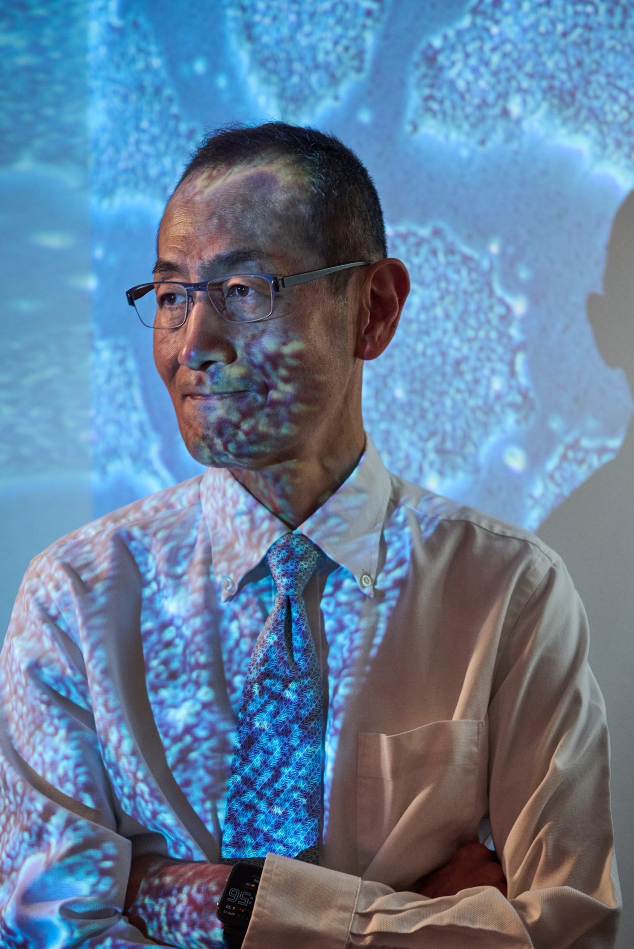 A man stands for a portrait in front of a blue projection.