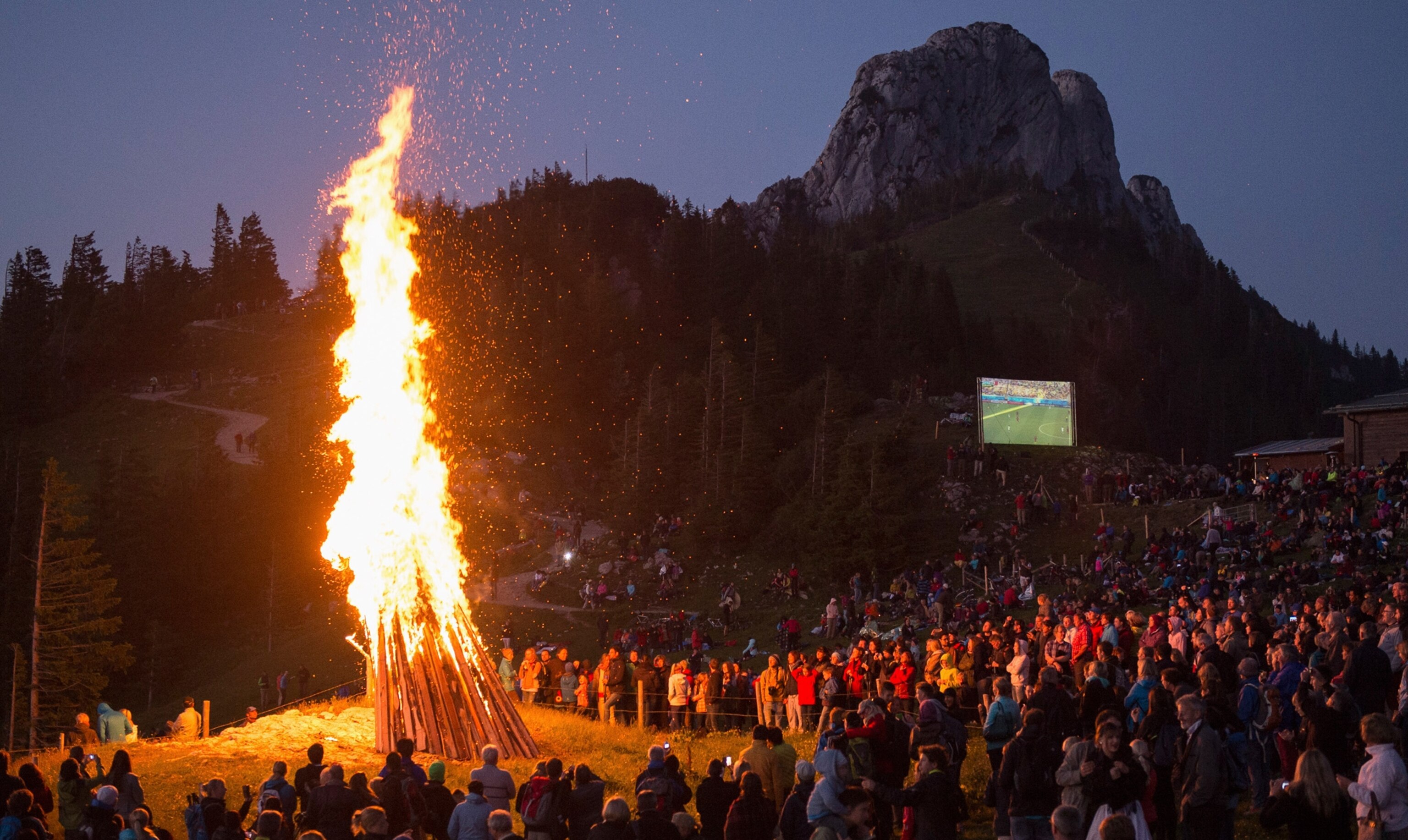 People gather around a bonfire and watch the 2014 World Cup Group G soccer match between Germany and Ghana on an outdoor film projector, during the Sonnwendfeuer (Midsummer) Festival at Mt. Kampenwand in Bavarian Alps, Germany.