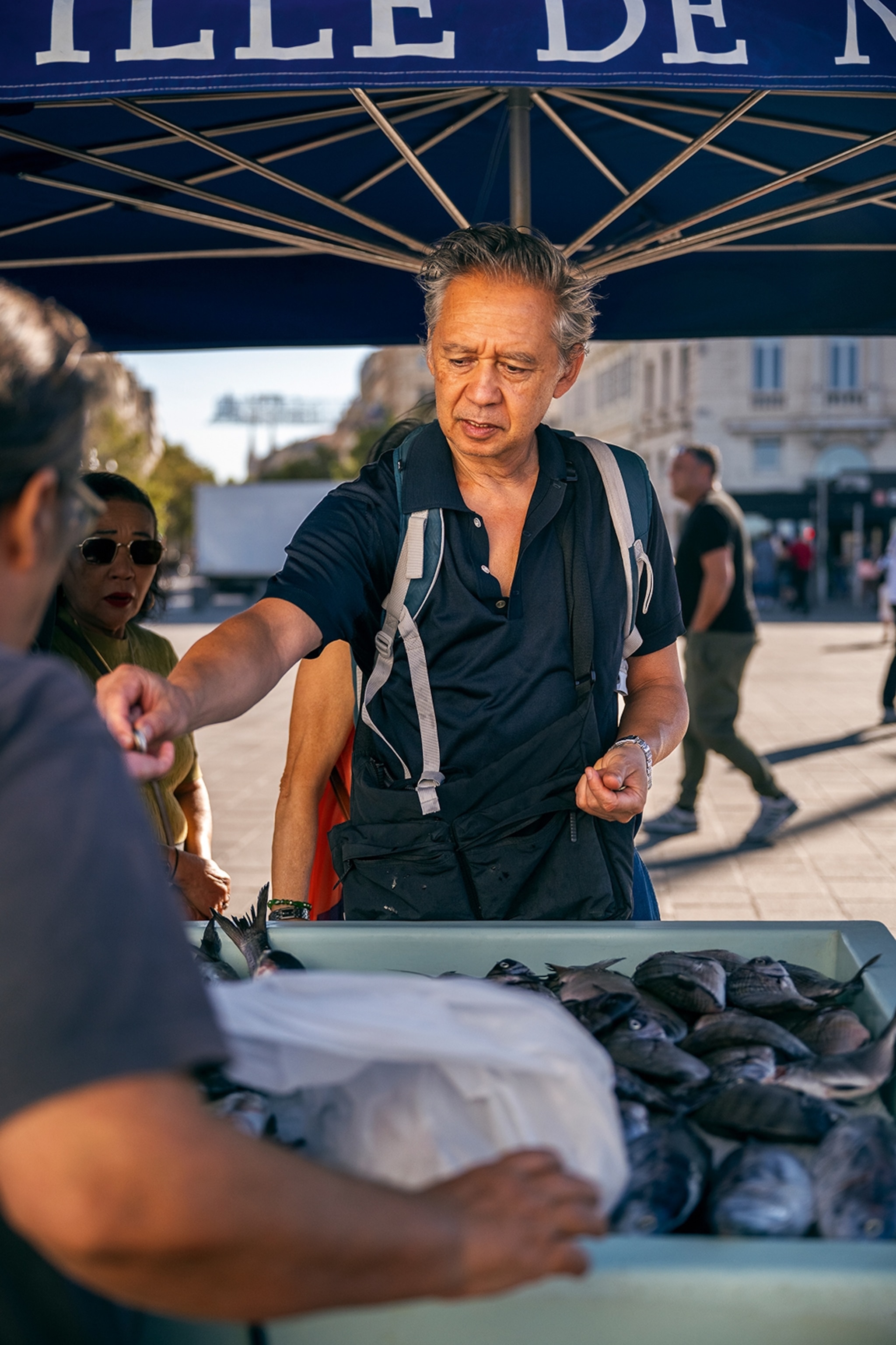 An older French man buying fish from a market at a harbour.