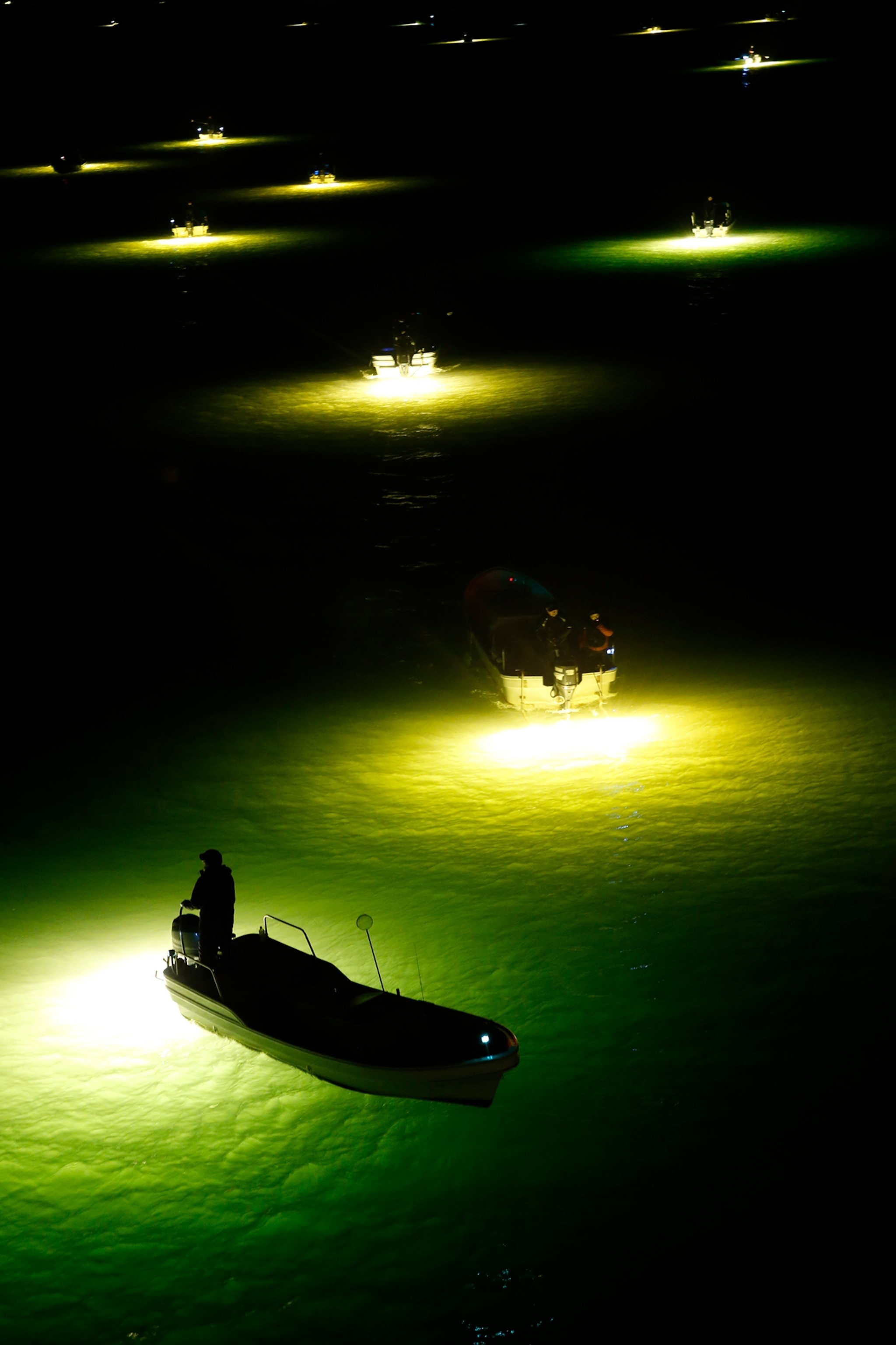 Fishermen look for glass eels from their boats with the light of fish lamps reflecting on the surface of the water in the estuary of the Yoshino River.