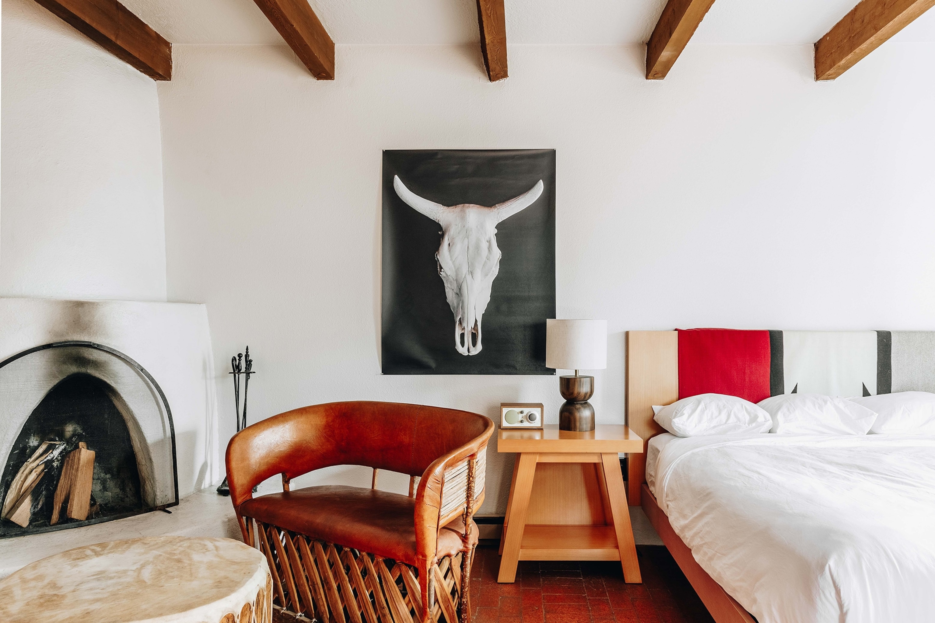 The interior of a stylish, modern hotel bedroom with a double bed, exposed beams on the ceiling an a painting of a bull skull hung on the wall.