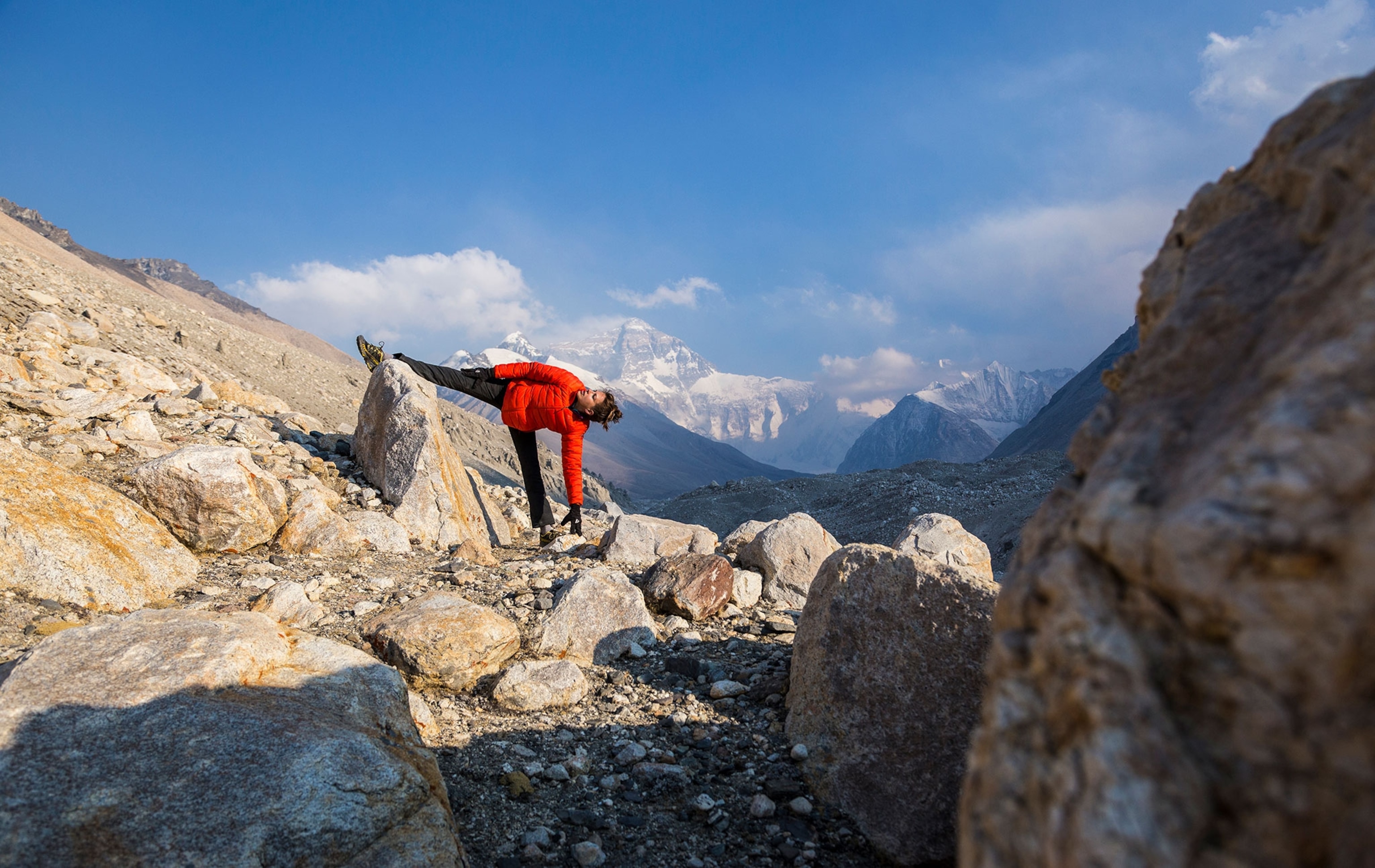 A woman stretches in the sun as high peaks appear through clouds near Everest Base Camp.