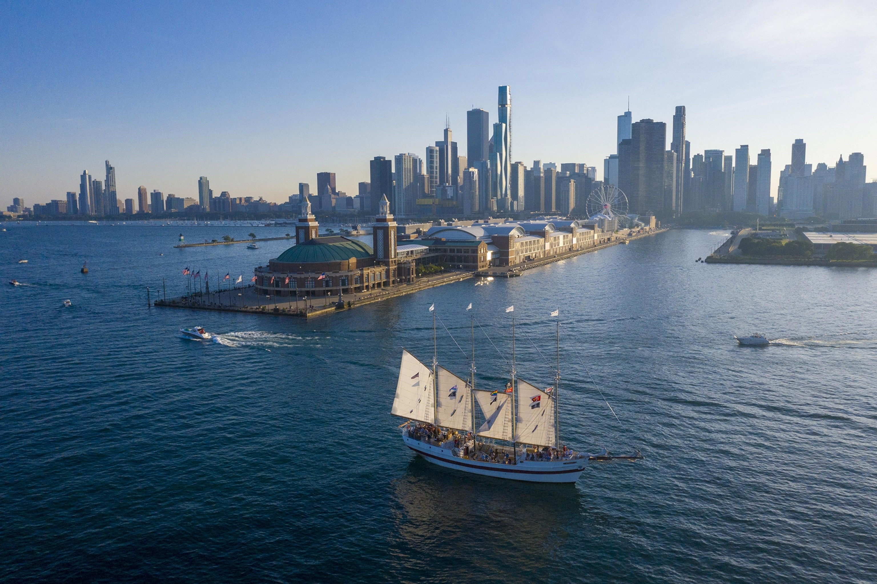 An aerial view of a sailboat floating near a long pier with a city skyline behind